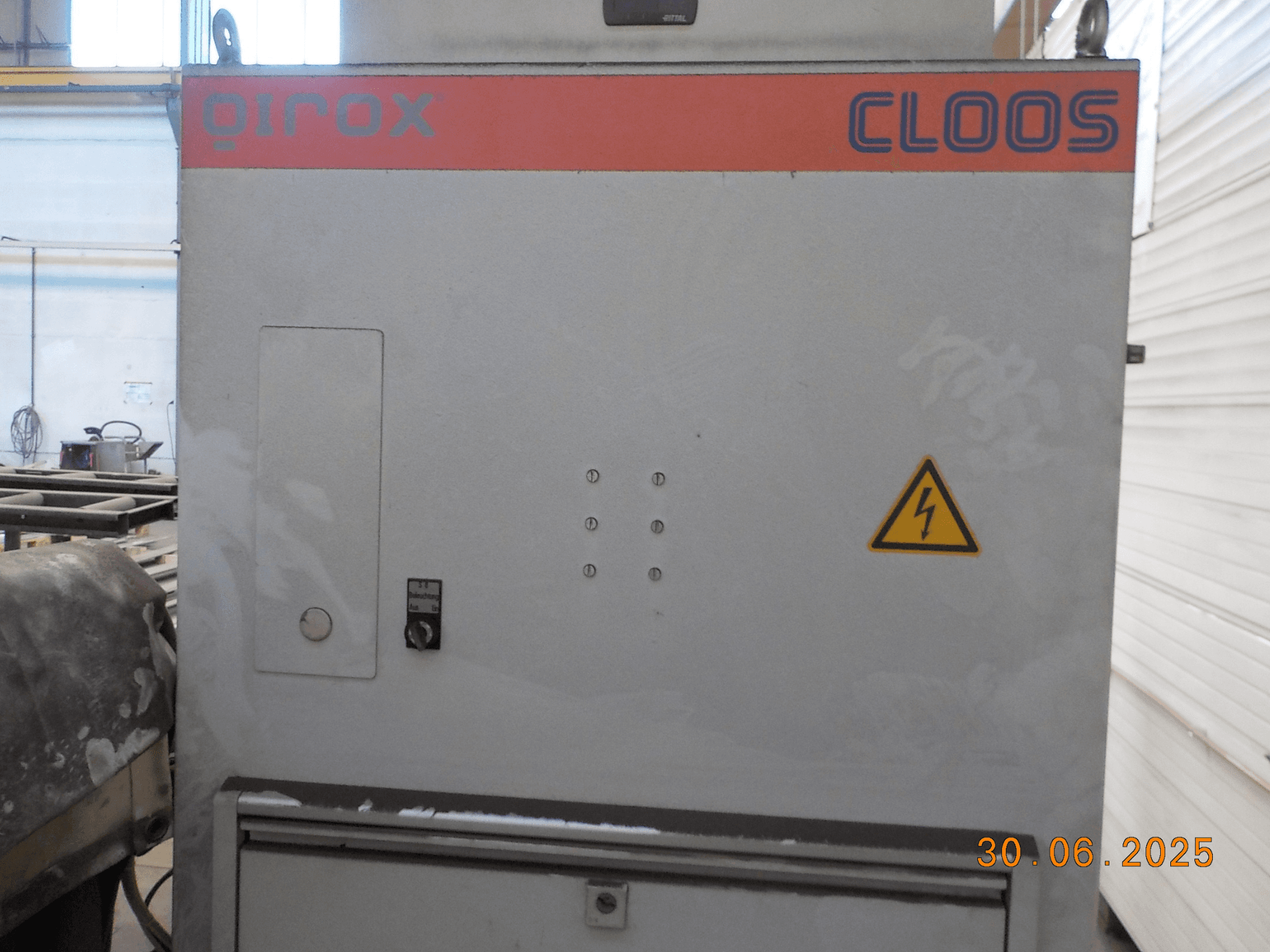 Zijaanzicht van Cloos QIROX lasmachine, met bedieningspaneel en waarschuwingsbord, met een stoffig oppervlak en zichtbare datumstempel.