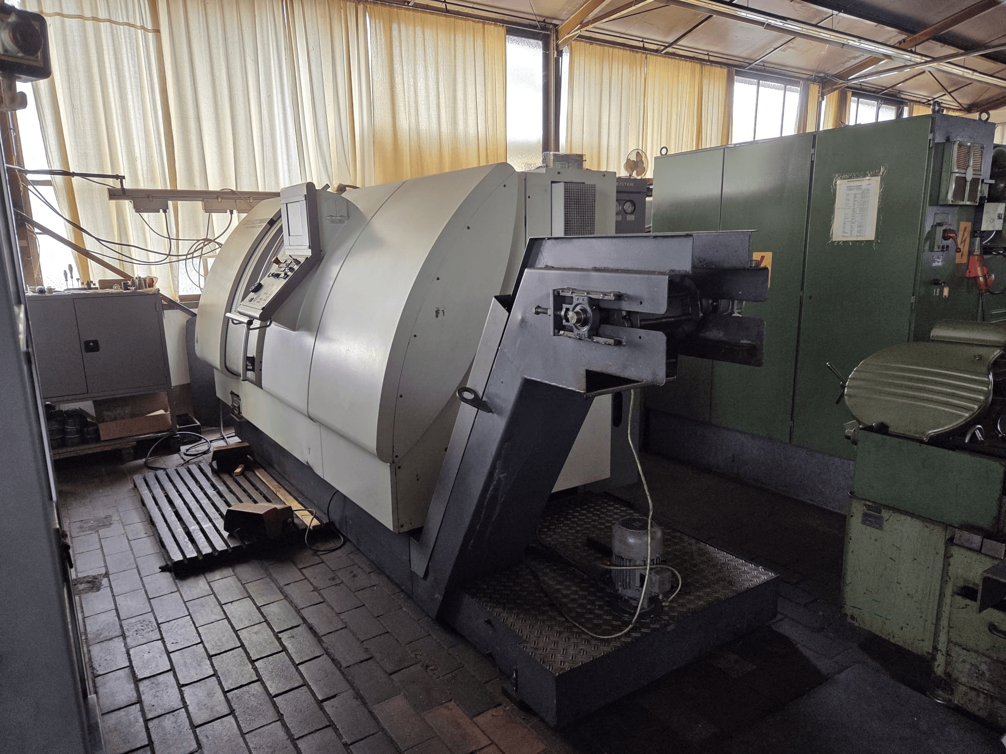 Gildemeister CTX 400 dubbel draai-freescentrum, zijaanzicht, met daarop het bedieningspaneel, het grote chassis en de aangrenzende machines in de werkplaats.