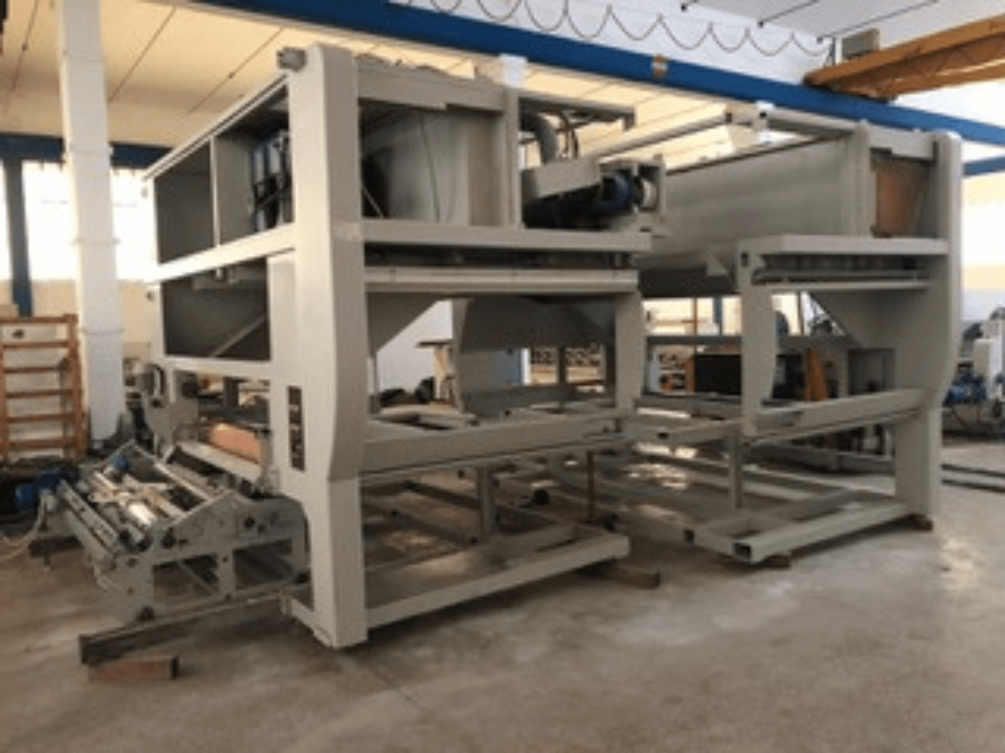 Industriële machine met meerdere transportrollen en grote structuur; zijaanzicht, grijze kleur, in een goed verlichte fabriek.