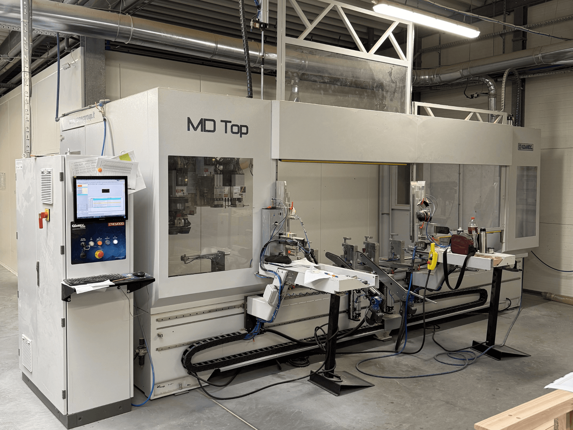 MD Top CNC machine gezien vanaf de voorkant, met een bedieningspaneel, robotarmen en een werkruimte met gereedschappen en materialen.