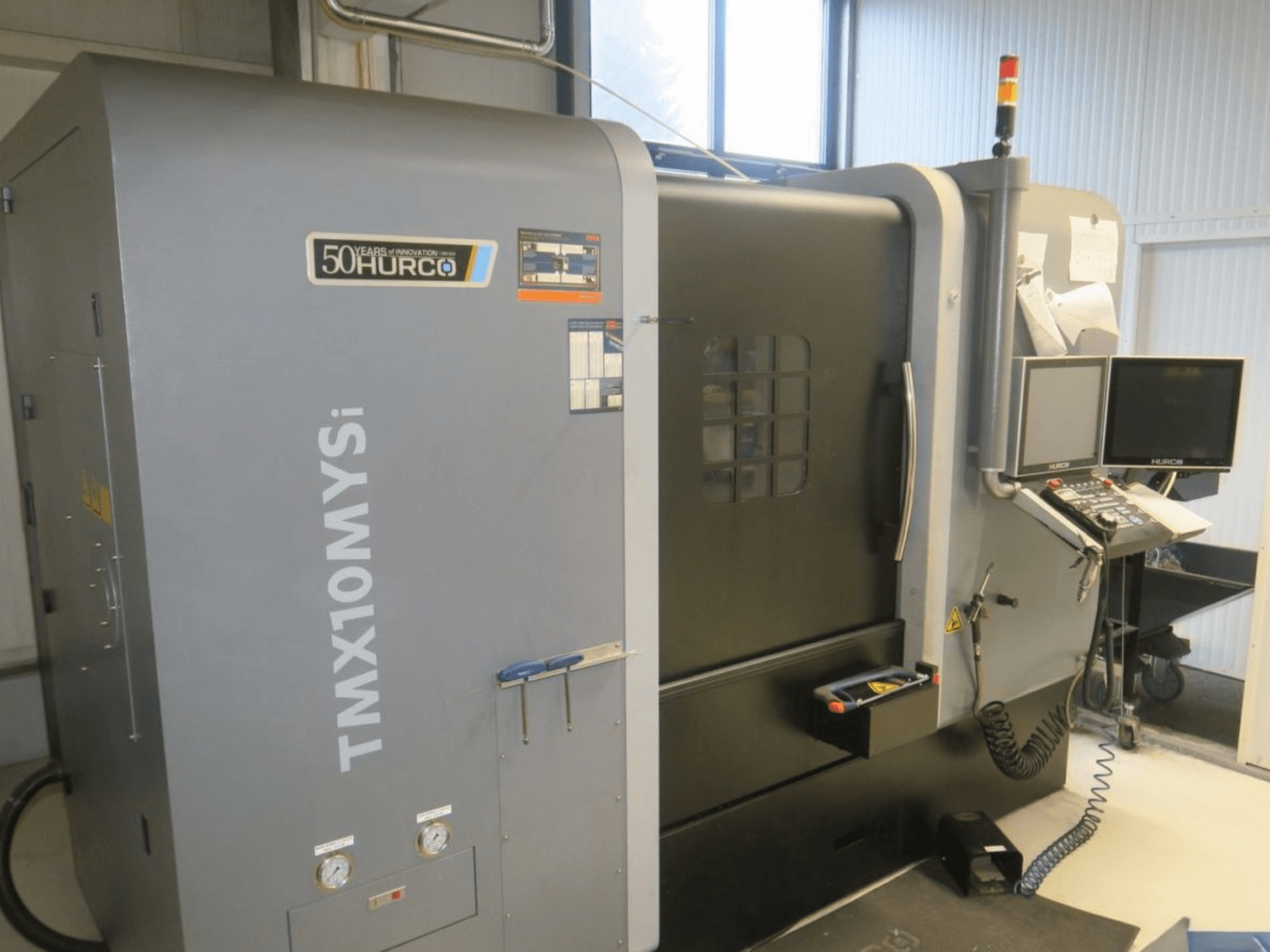 Hurco TMX10MYSi CNC machine in zijaanzicht; met bedieningspaneel, noodverlichting en getoonde meters.