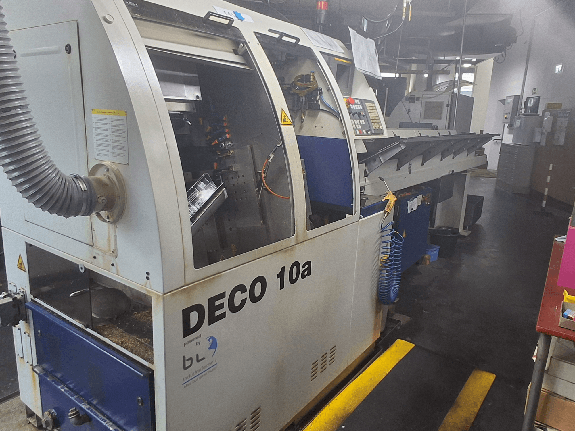 Zwitserse draaimachine TORNOS DECO 10a, vooraanzicht; heeft een bedieningspaneel, zichtbare mechanismen en een buis voor stofafzuiging.