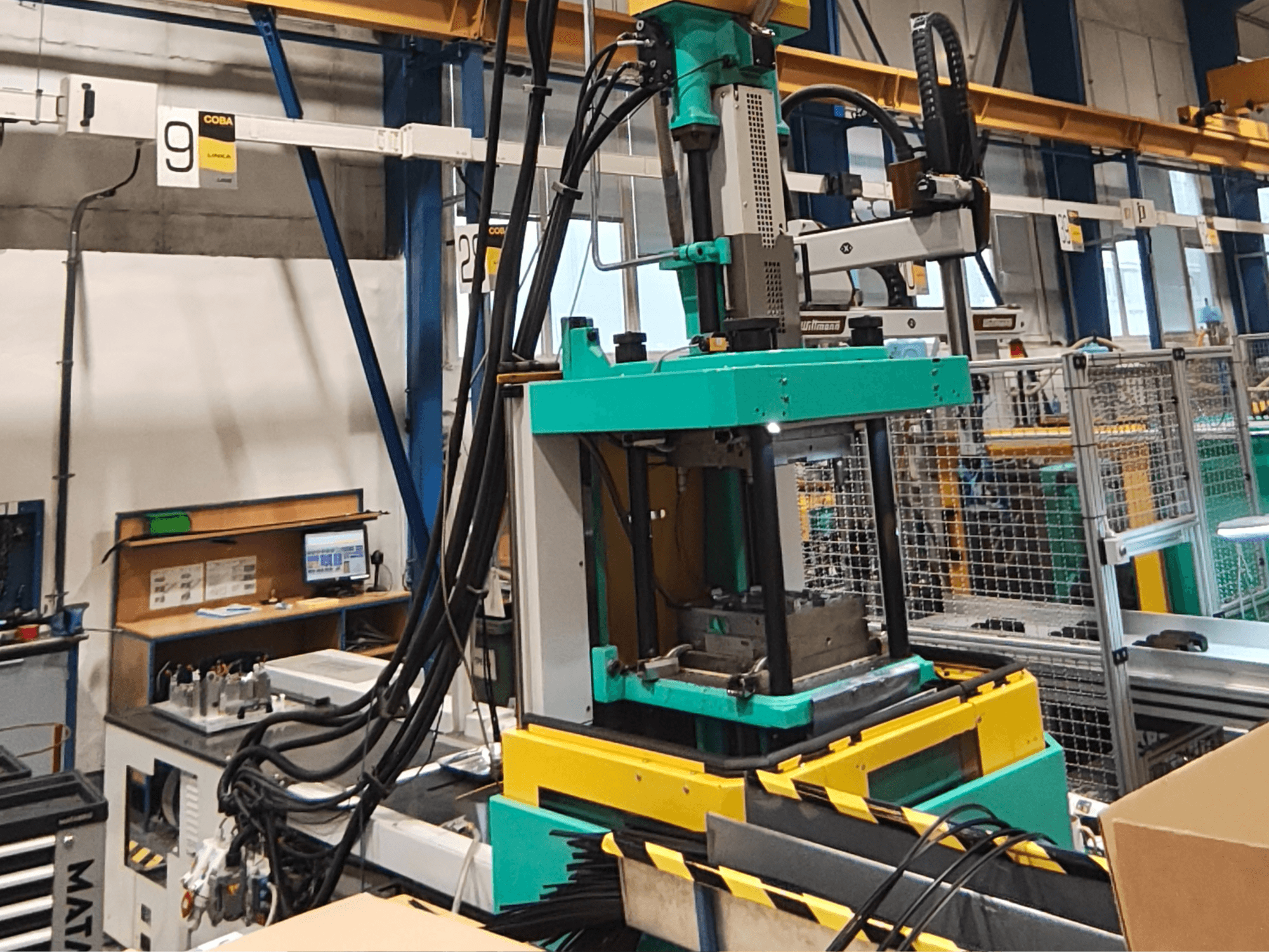 Groen met gele hydraulische persmachine in een fabriek, vooraanzicht, met zichtbaar bedieningspaneel en kabels aan de zijkant.