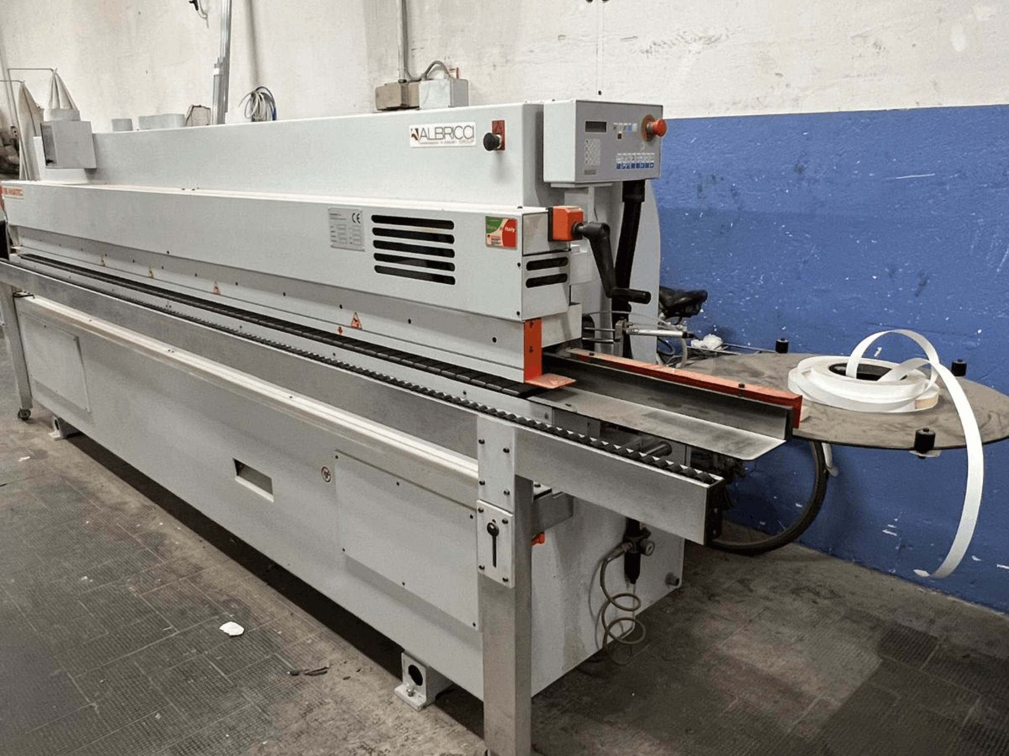 ALBRICO kantenaanlijmmachine met vooraanzicht, met een lange transportband en een bevestigde rol plakband.