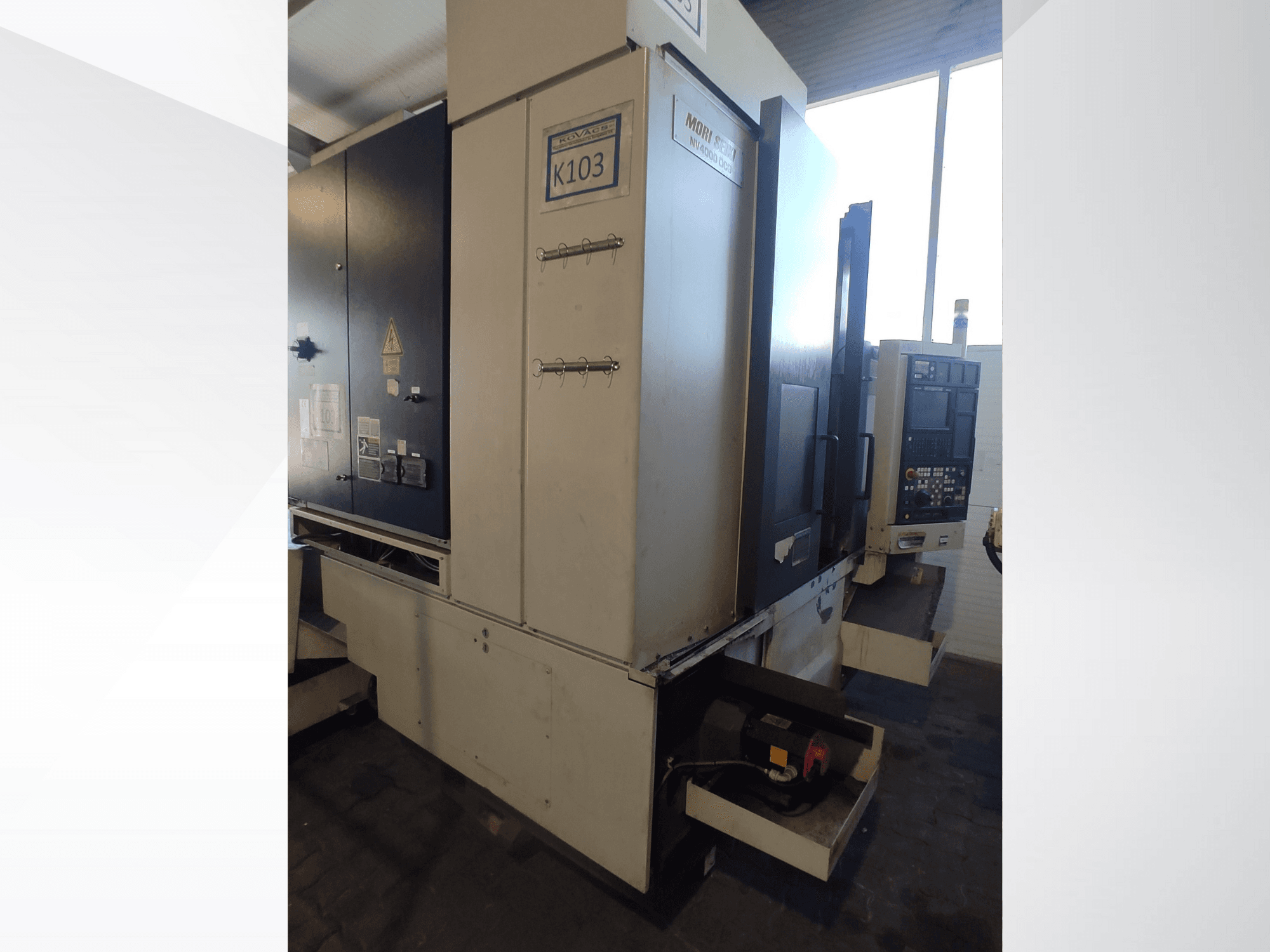 Mori Seiki K103 CNC machine in vooraanzicht, met bedieningspaneel, veiligheidslabels en elektrische componenten zichtbaar.