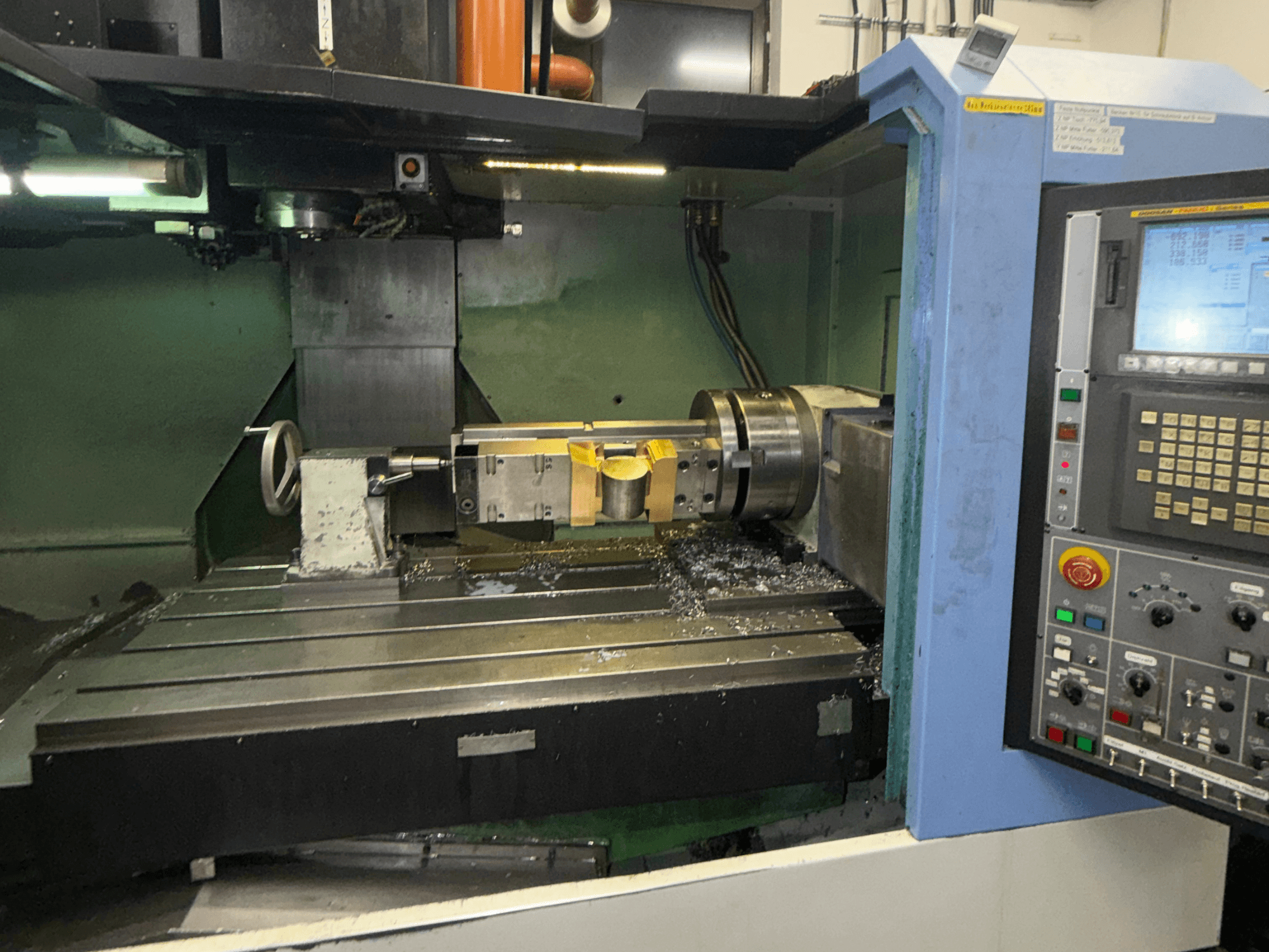 DOOSAN DNM650 verticaal bewerkingscentrum, vooraanzicht, met het snijgereedschap en het bedieningspaneel in beeld, en metaalkrullen zichtbaar op de tafel.