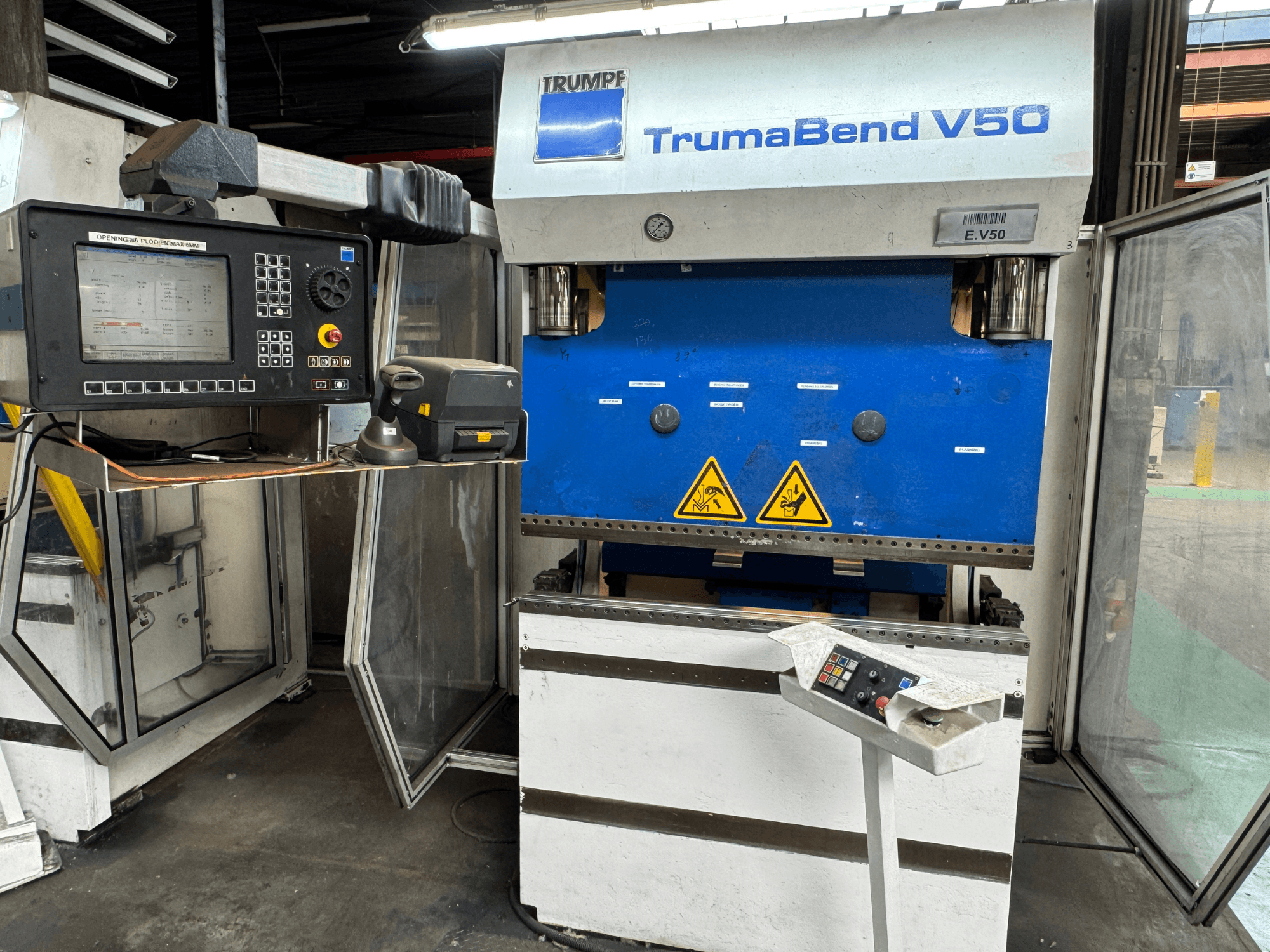 De TRUMPF TrumaBend V50 afkantpers in vooraanzicht, met een bedieningspaneel, veiligheidswaarschuwingen en een opvallend blauw-wit ontwerp.