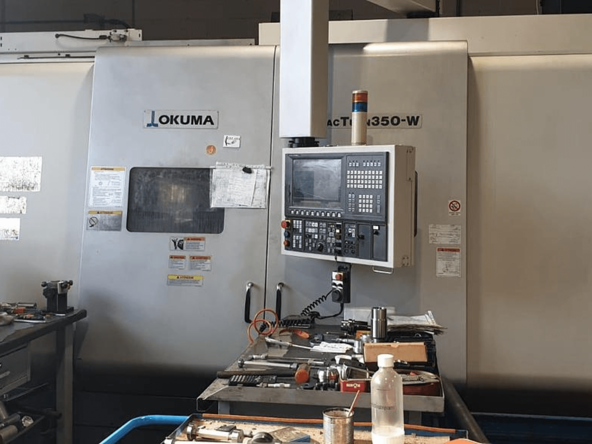 Okuma MAC TURN 350-W draaifreescentrum, vooraanzicht met bedieningspaneel en werkruimte vol met gereedschap en een fles.