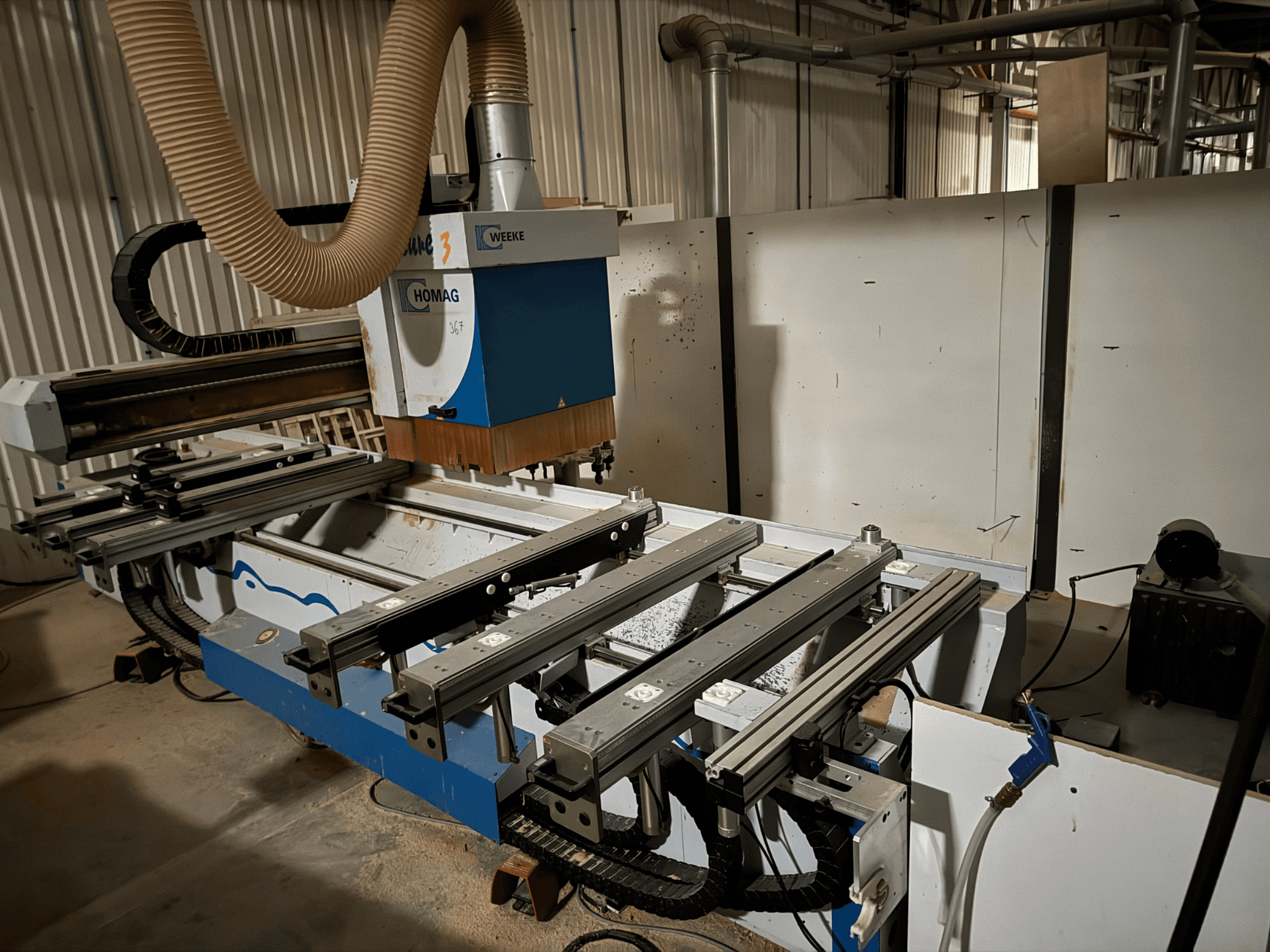 HOMAG CNC machine met een blauw en wit ontwerp, zijaanzicht, voorzien van schuifrails, een stofafzuigsysteem en gemonteerde gereedschappen.