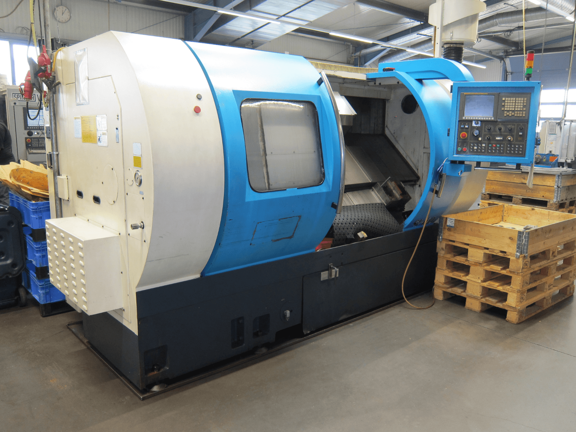 Johnford SL60 horizontale draaimachine, zijaanzicht, met het bedieningspaneel en interieur, met houten pallets vlakbij.