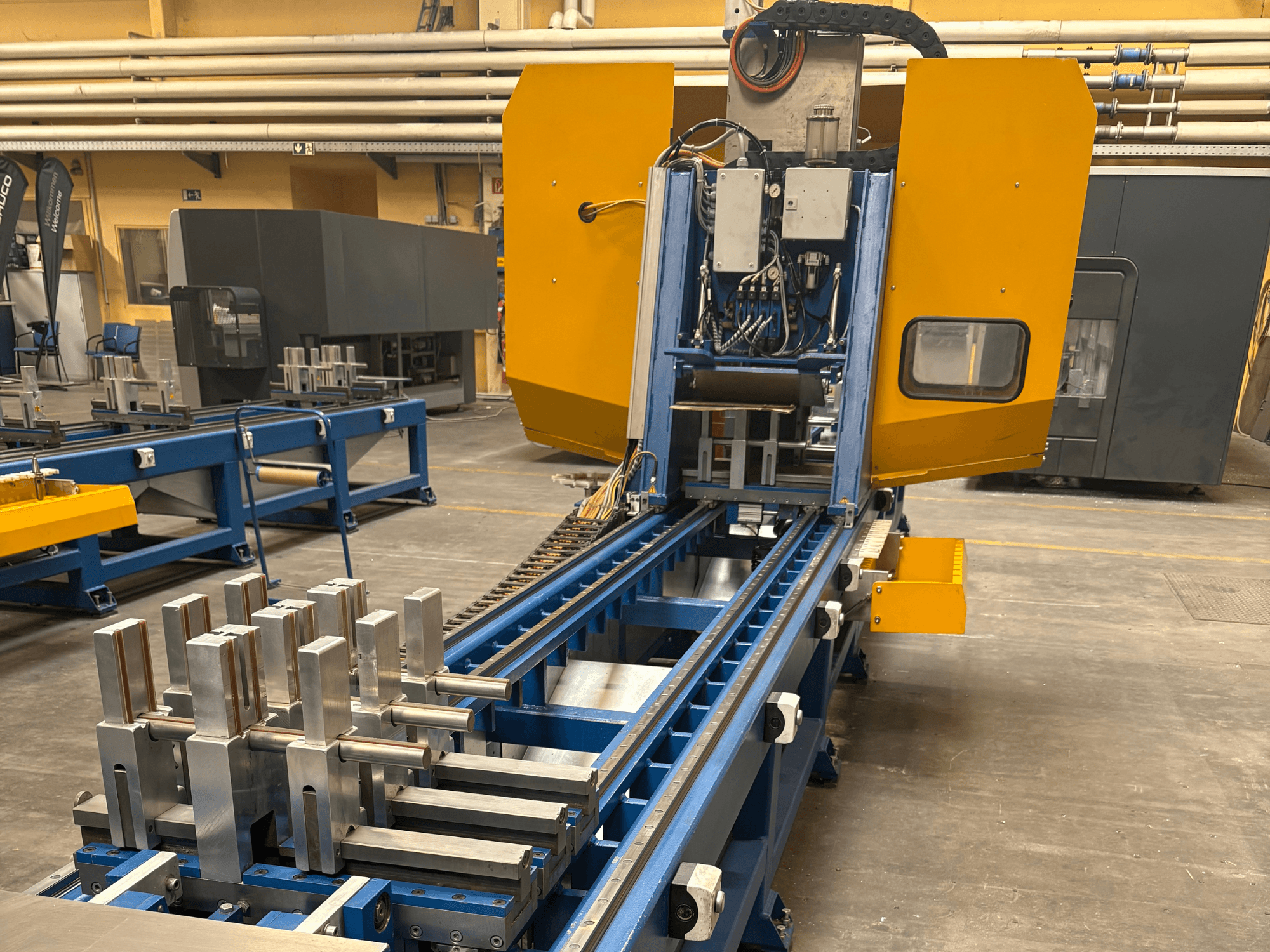 Vooraanzicht van het universeel bewerkingscentrum SCHÜCO PBX AL, met metalen werkstukken op een blauw bewerkingsbed.