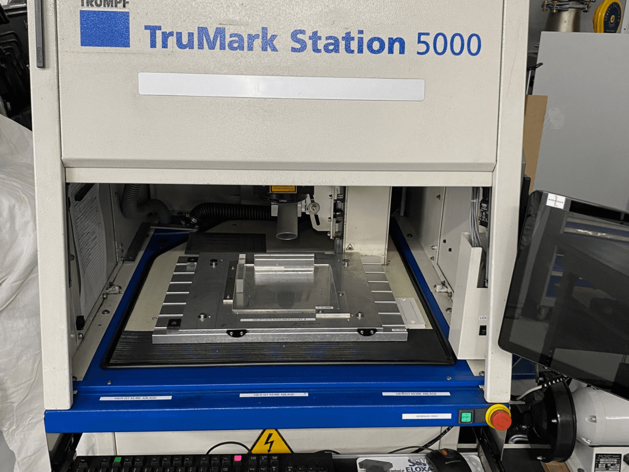 Vooraanzicht van de TruMark Station 5000 lasermarkeermachine met werktafel, bedieningselementen en monitoringscherm.