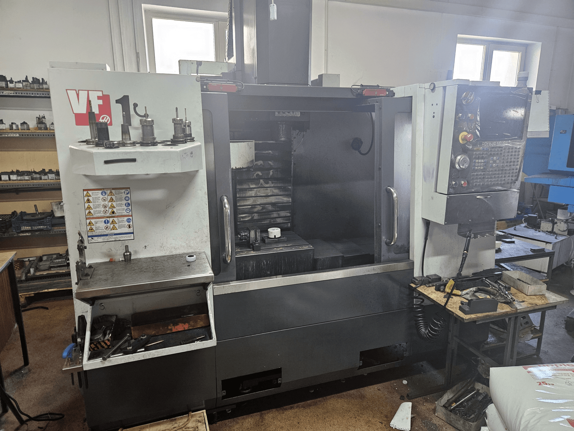 HAAS VF-1 verticaal bewerkingscentrum, vooraanzicht met gereedschap aan de zijkant, bedieningspaneel zichtbaar en werkruimte op de achtergrond.