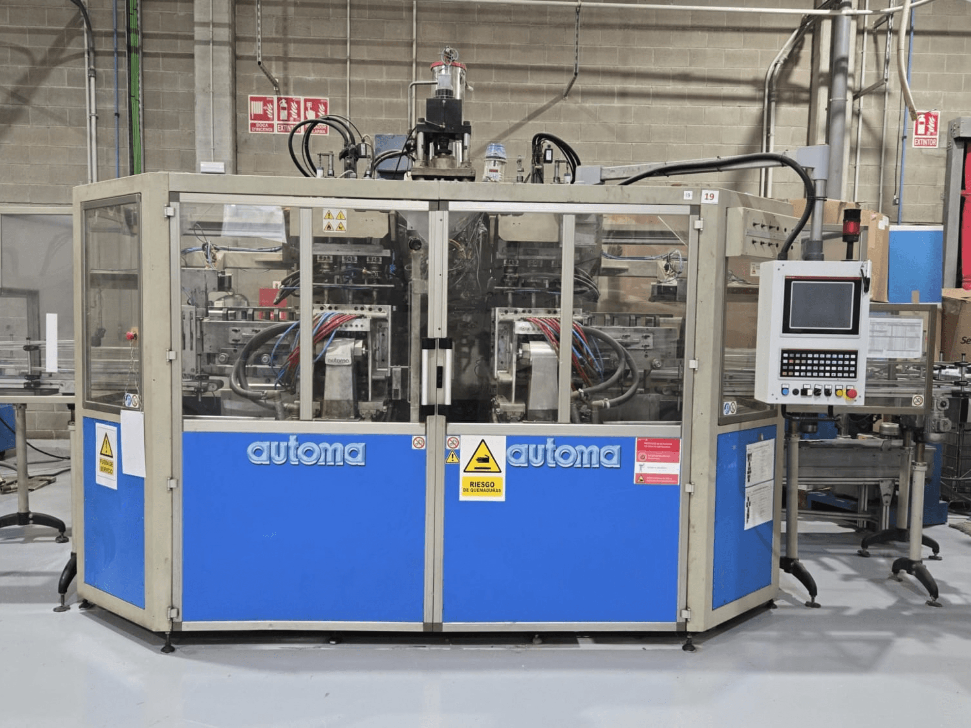 Vooraanzicht van de AUTOMA APEX AT500D blaasvormmachine, met bedieningspaneel en diverse slangen, in een fabrieksomgeving.