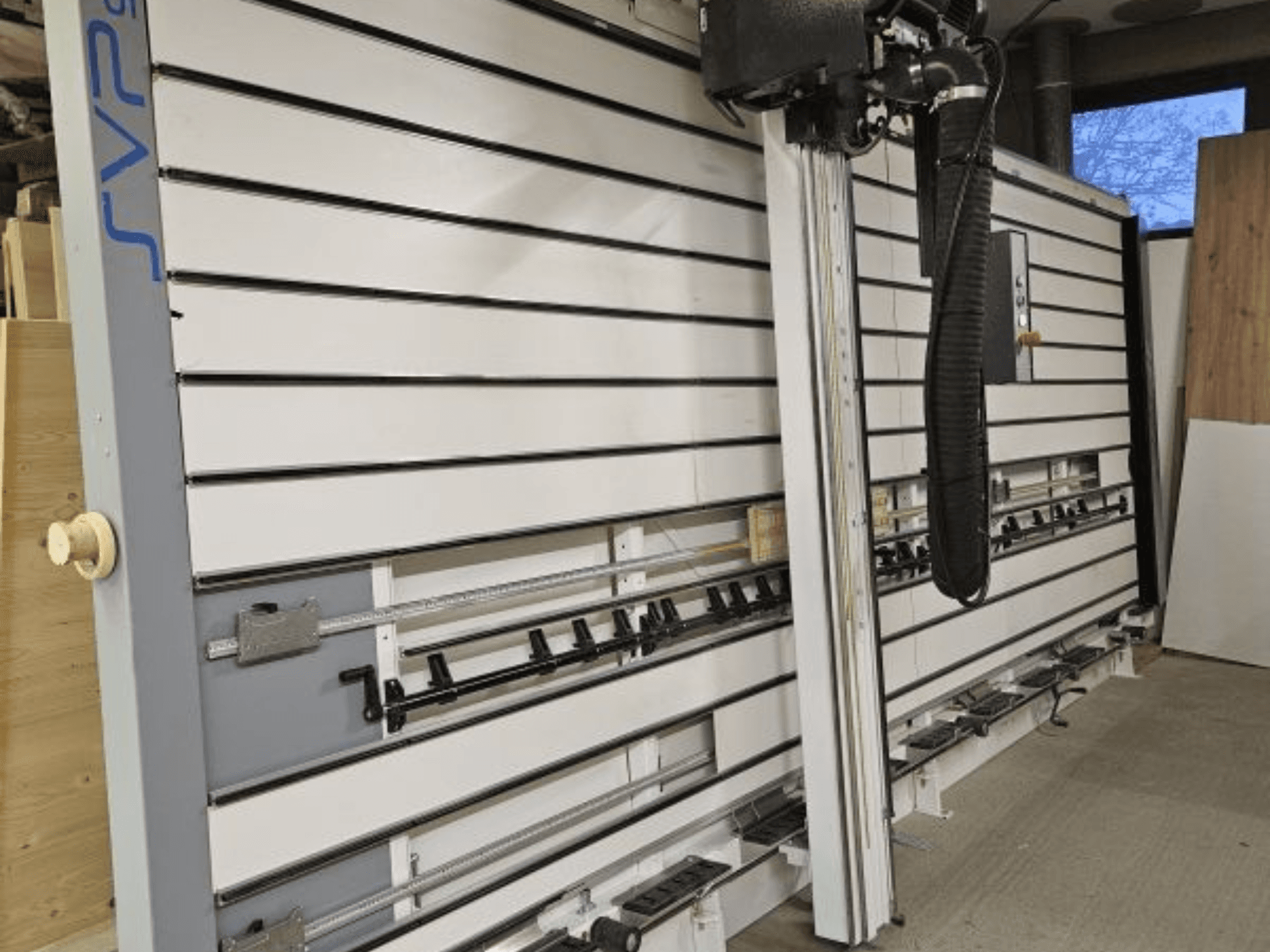 SVP schuifpaneelzaag in een werkplaats, vooraanzicht, met verstelbare rupsbanden en een stofafzuigsysteem boven het hoofd.