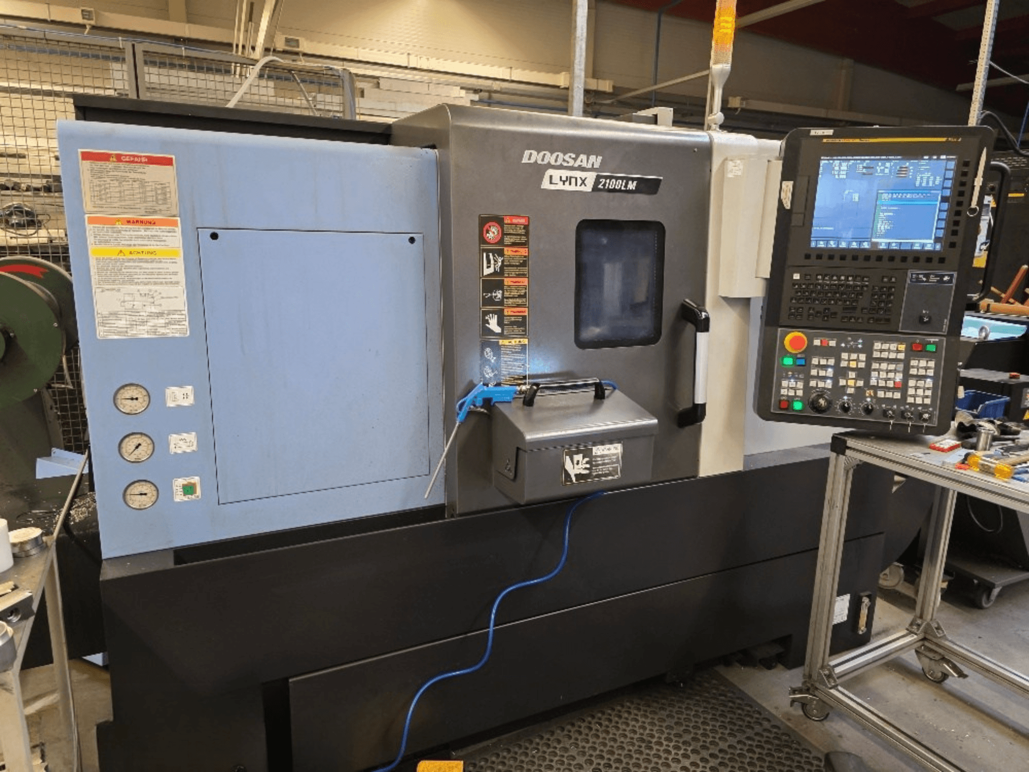 Doosan Lynx 2100LM CNC draaibank, vooraanzicht, met bedieningspaneel, drukmeters en veiligheidswaarschuwingen.