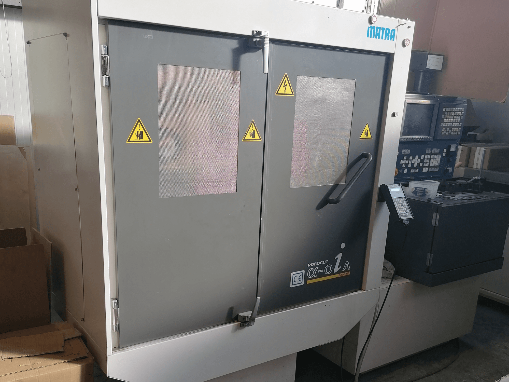 Robocut α-oZα machine van Matra, vooraanzicht met veiligheidswaarschuwingen, bedieningspaneel en dubbele deuren met gaasramen.