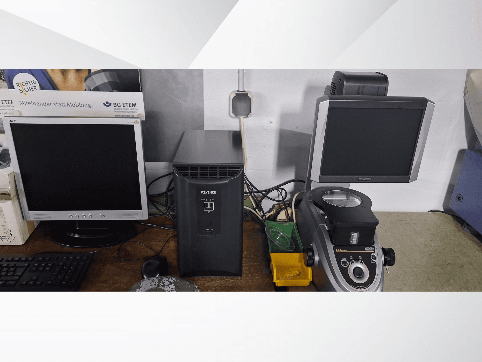 Twee computermonitoren, een Acer en een Keyence, naast een zwart apparaat en een microscoop, gezien vanaf de voorkant.