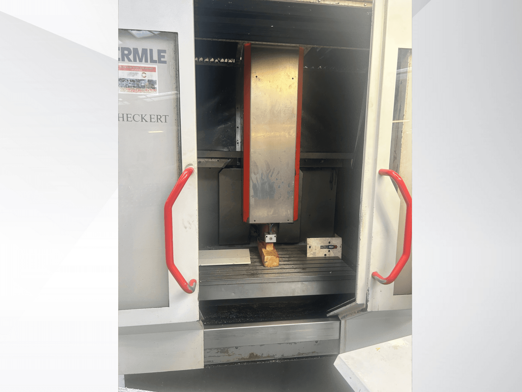 Hermle CNC machine vooraanzicht, met een metalen interieur, rode handgrepen en een werkstuk op de tafel.