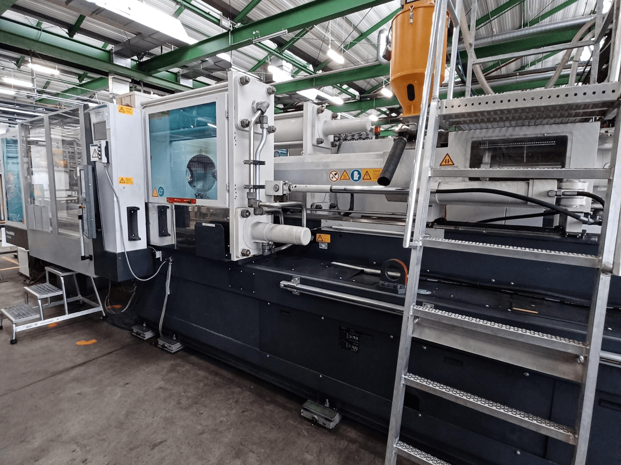 Industriële spuitgietmachine met een duidelijk vooraanzicht waarop de merktekens, het bedieningspaneel en de materiaaltrechter te zien zijn.