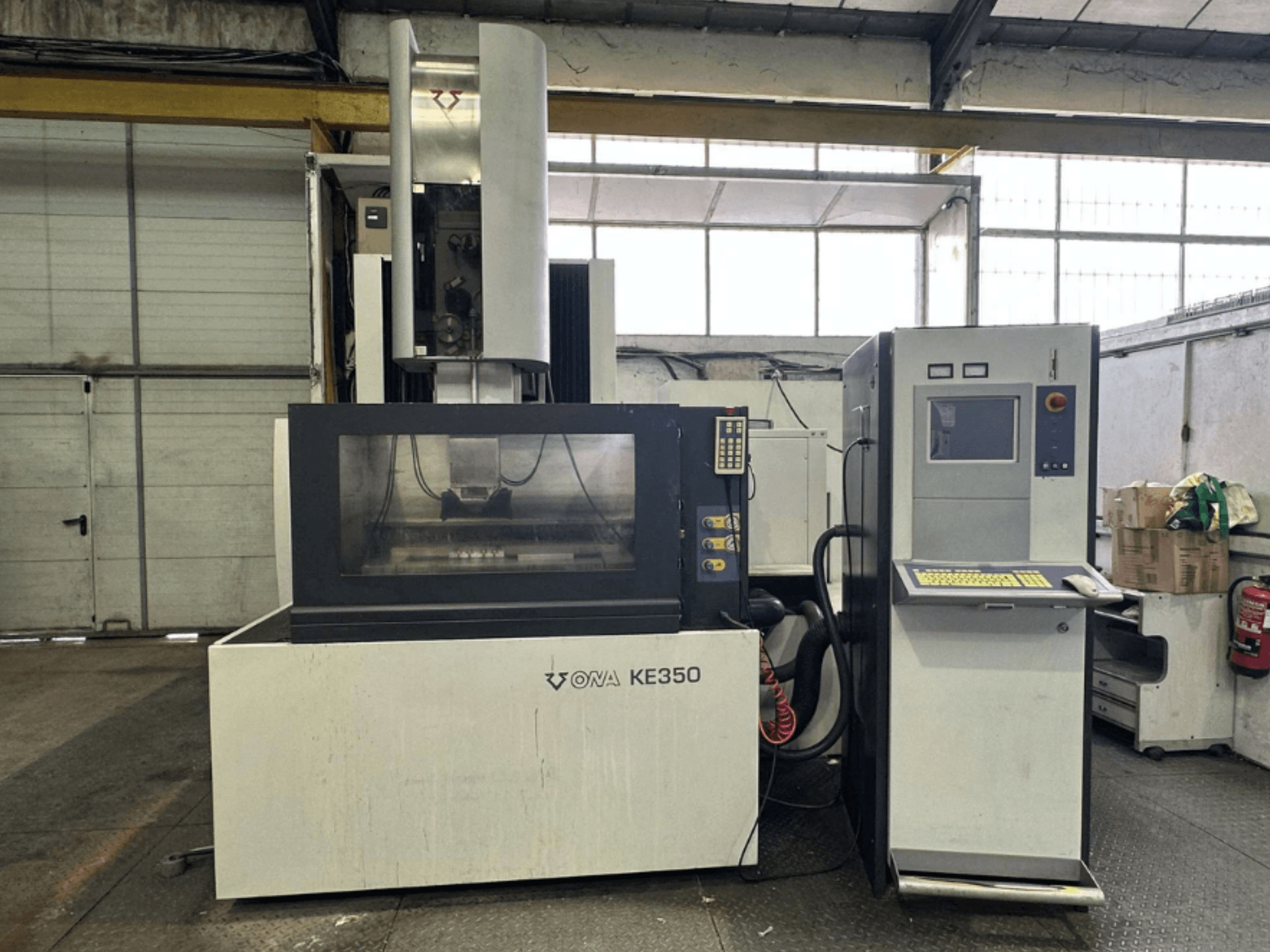 Vooraanzicht van de ONA KE350 CNC machine met bedieningspaneel, scherm en diverse knoppen, in een industriële omgeving.