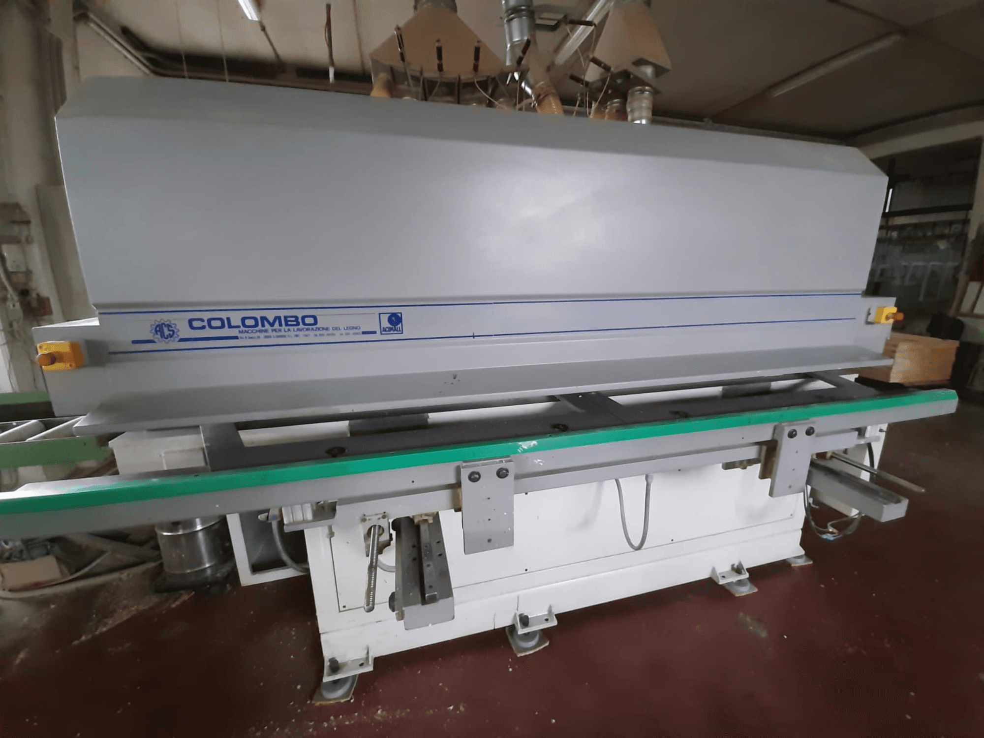 Colombo houtverwerkingsmachine, vooraanzicht, met een lange groene tafel, bedieningsknoppen en een grijze behuizing met blauwe accenten.