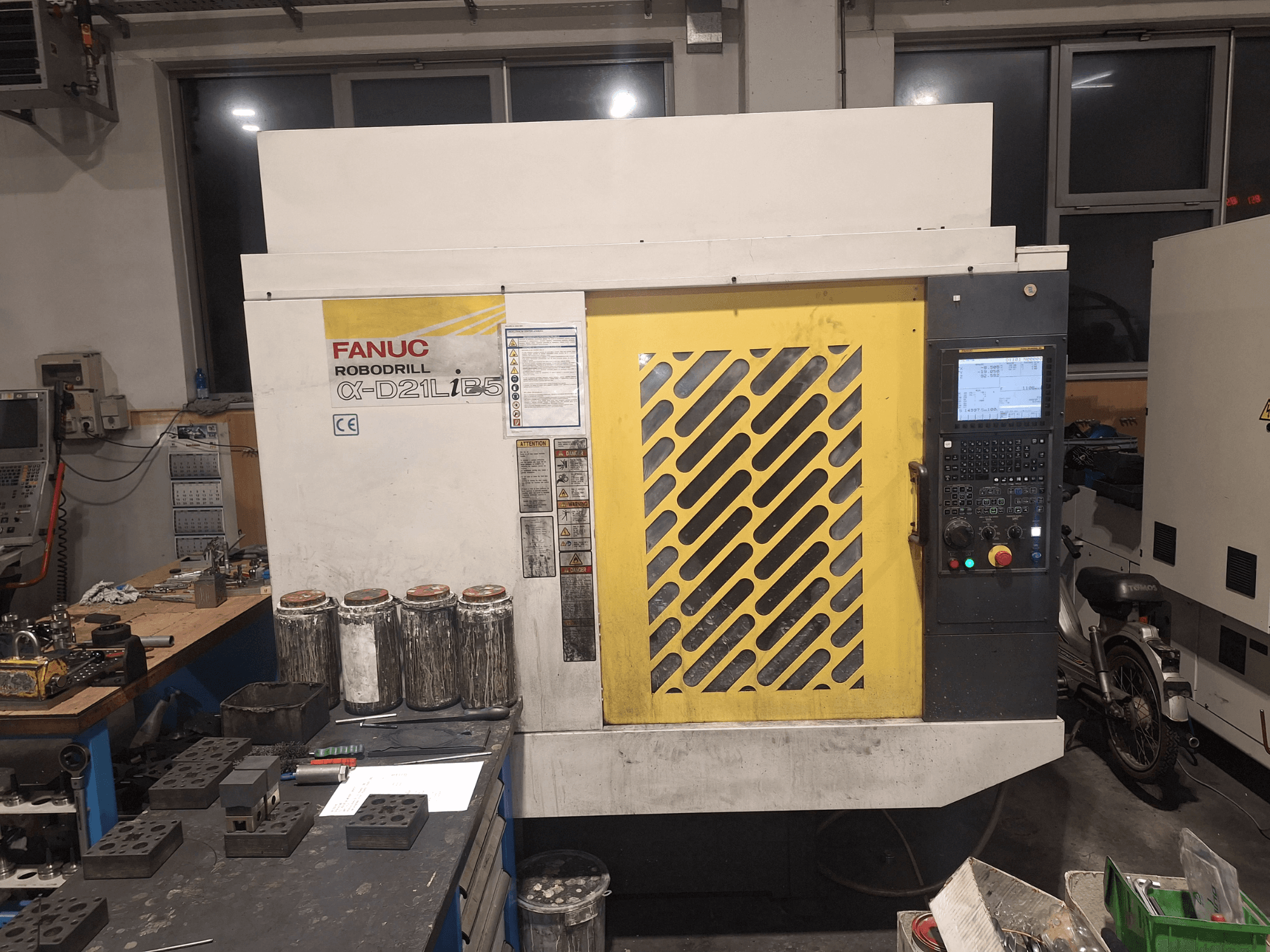 Vooraanzicht van de FANUC Robodrill α-D21LiB5, met het bedieningspaneel, het gele rooster en de nabijgelegen gereedschappen op een werkbank.