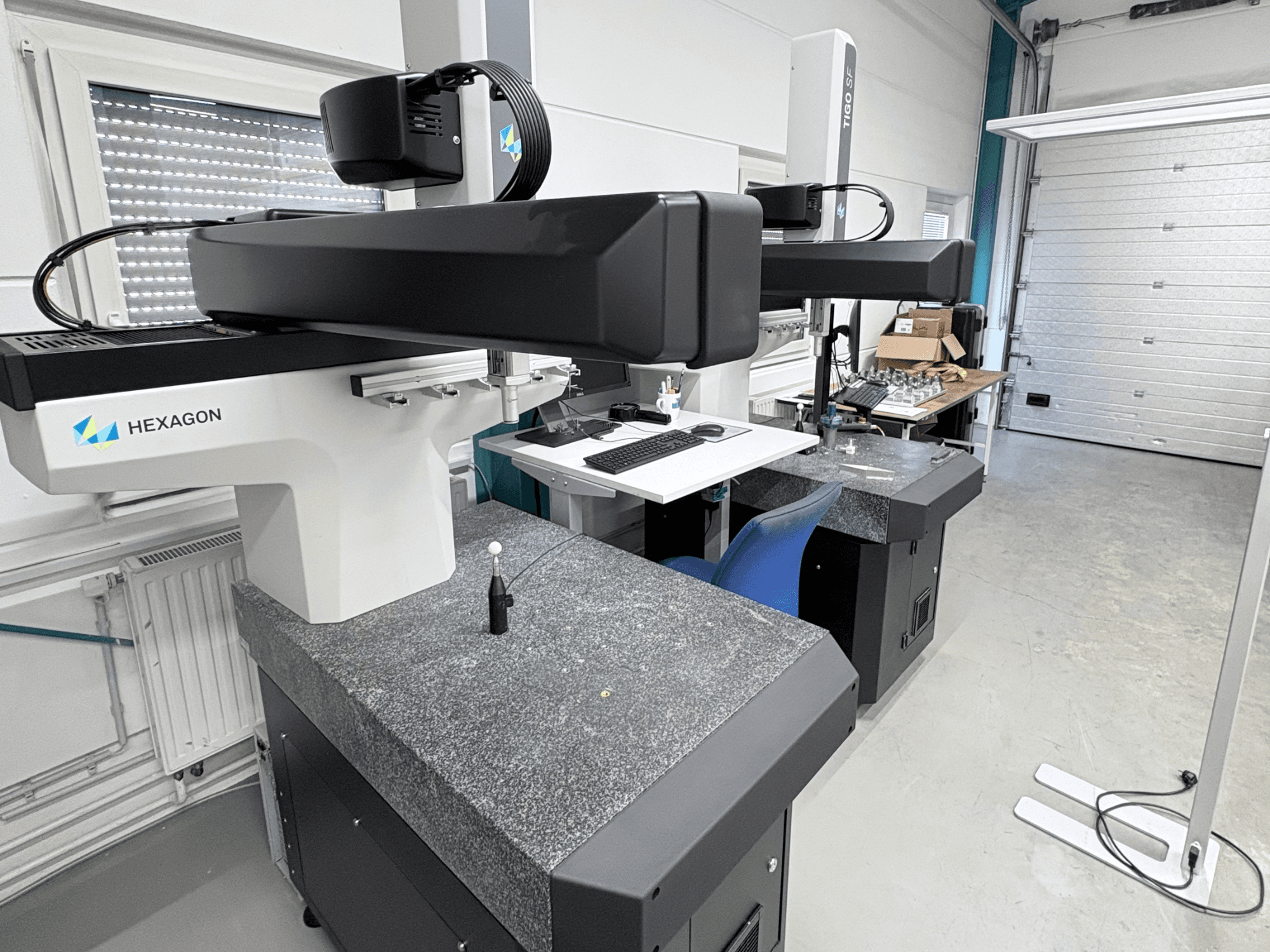 Hexagon Tigo SF CMM in de werkplaats, voorzien van een granieten basis, een meetsonde en een werkplek met gereedschap in de buurt.