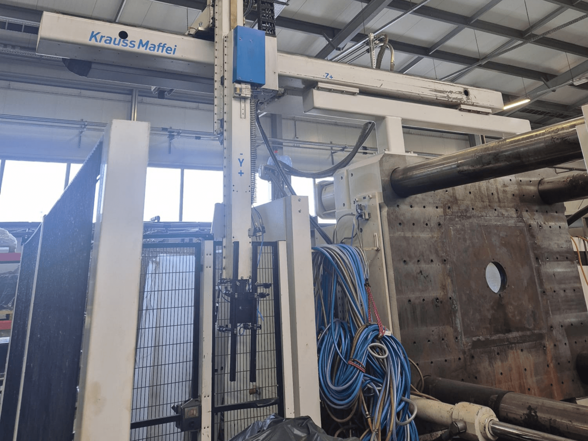 Krauss Maffei 1300-12000 MX hydraulische spuitgietmachine, vooraanzicht met mechanische armen en hydraulische aansluitingen.
