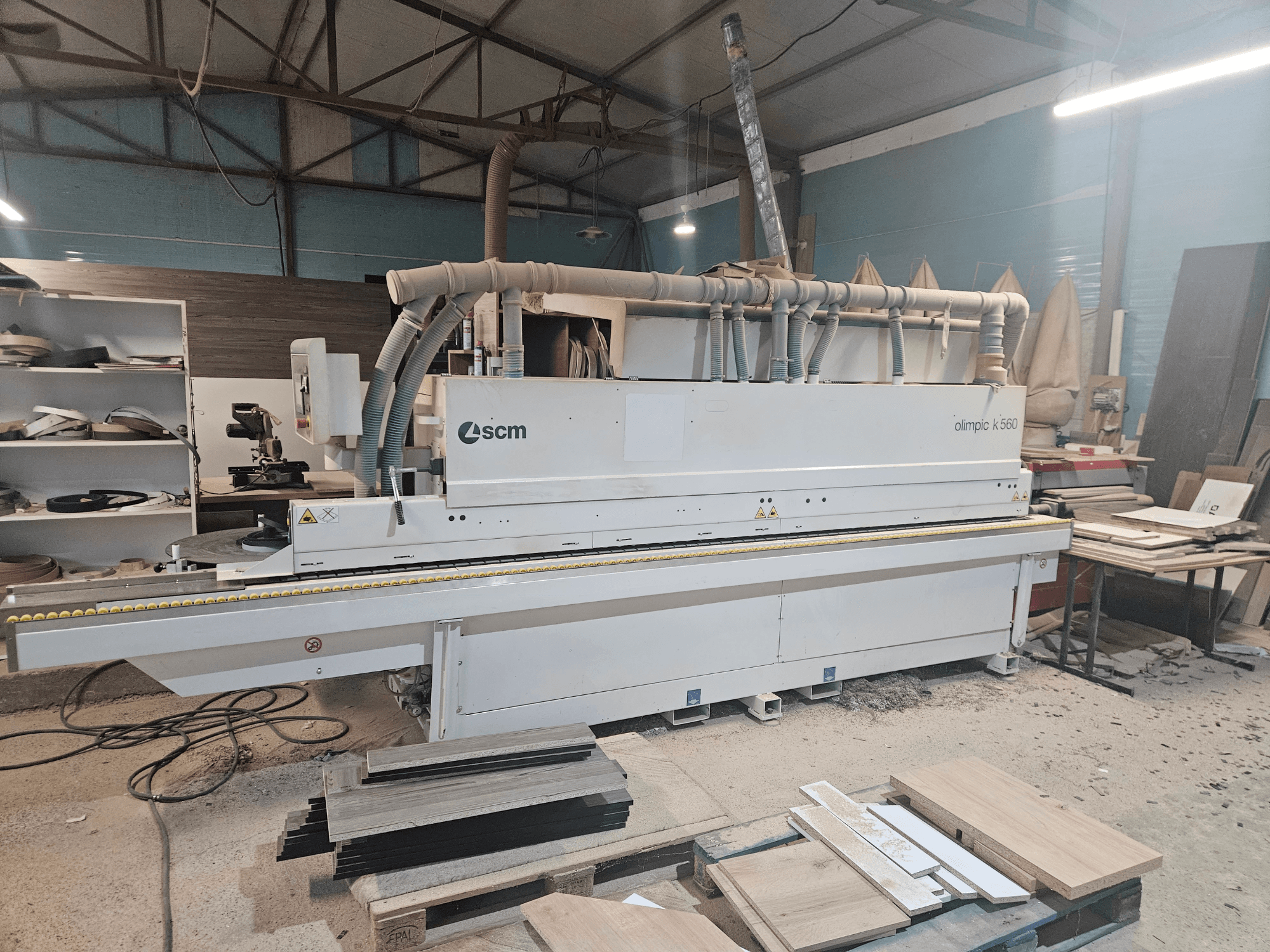 SCM Olimpic K560 kantenaanlijmmachine in een werkplaats, vooraanzicht, met houten panelen en gereedschap zichtbaar op de vloer.