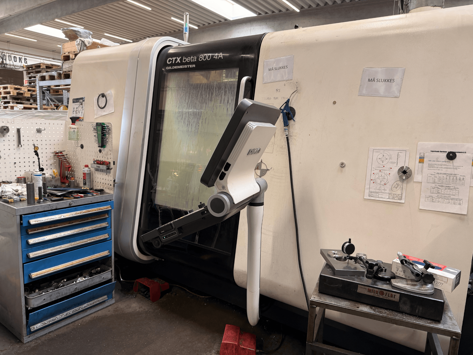 DMG MORI CTX Beta 800 4a verticale draaimachine in een werkplaats, met een bedieningsarm en technische documenten in de buurt.