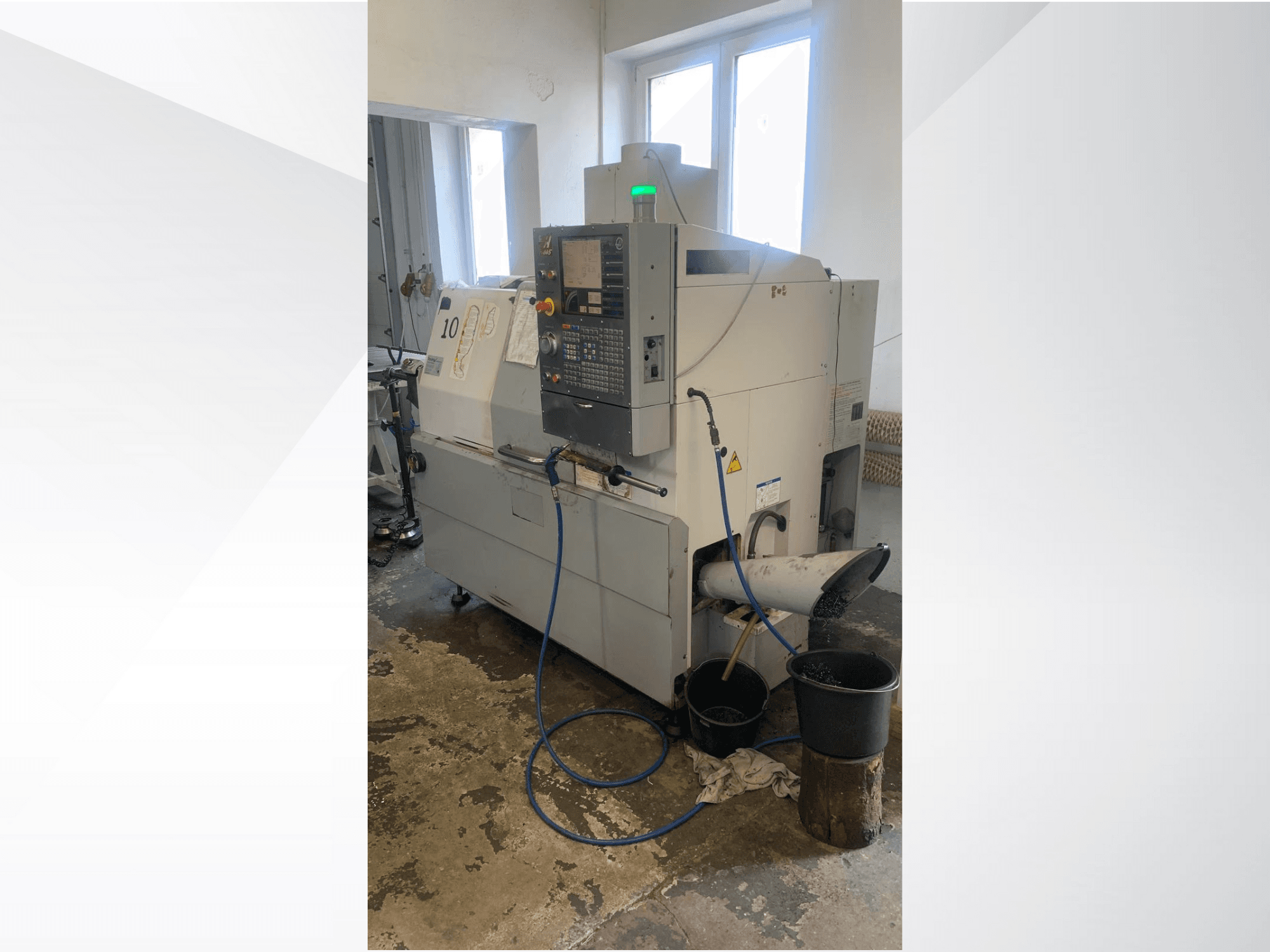 Haas CNC machinemodel met bedieningspaneel, zijaanzicht, met koelmiddelleiding, afvoergoot en opslagcontainers eronder.