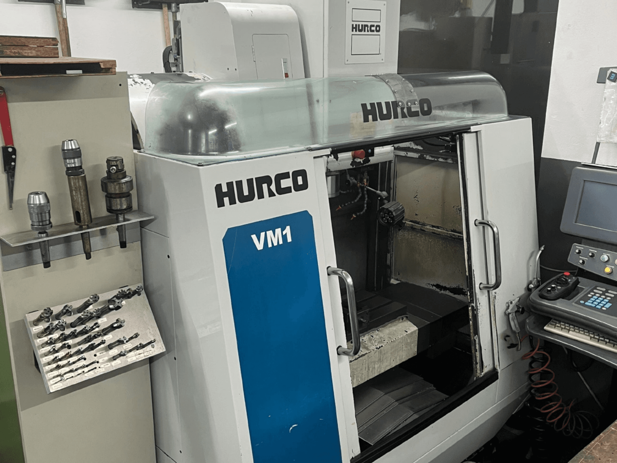 Vooraanzicht Hurco VM1 verticaal bewerkingscentrum, met transparante kap, bedieningspaneel en gemonteerde gereedschappen.