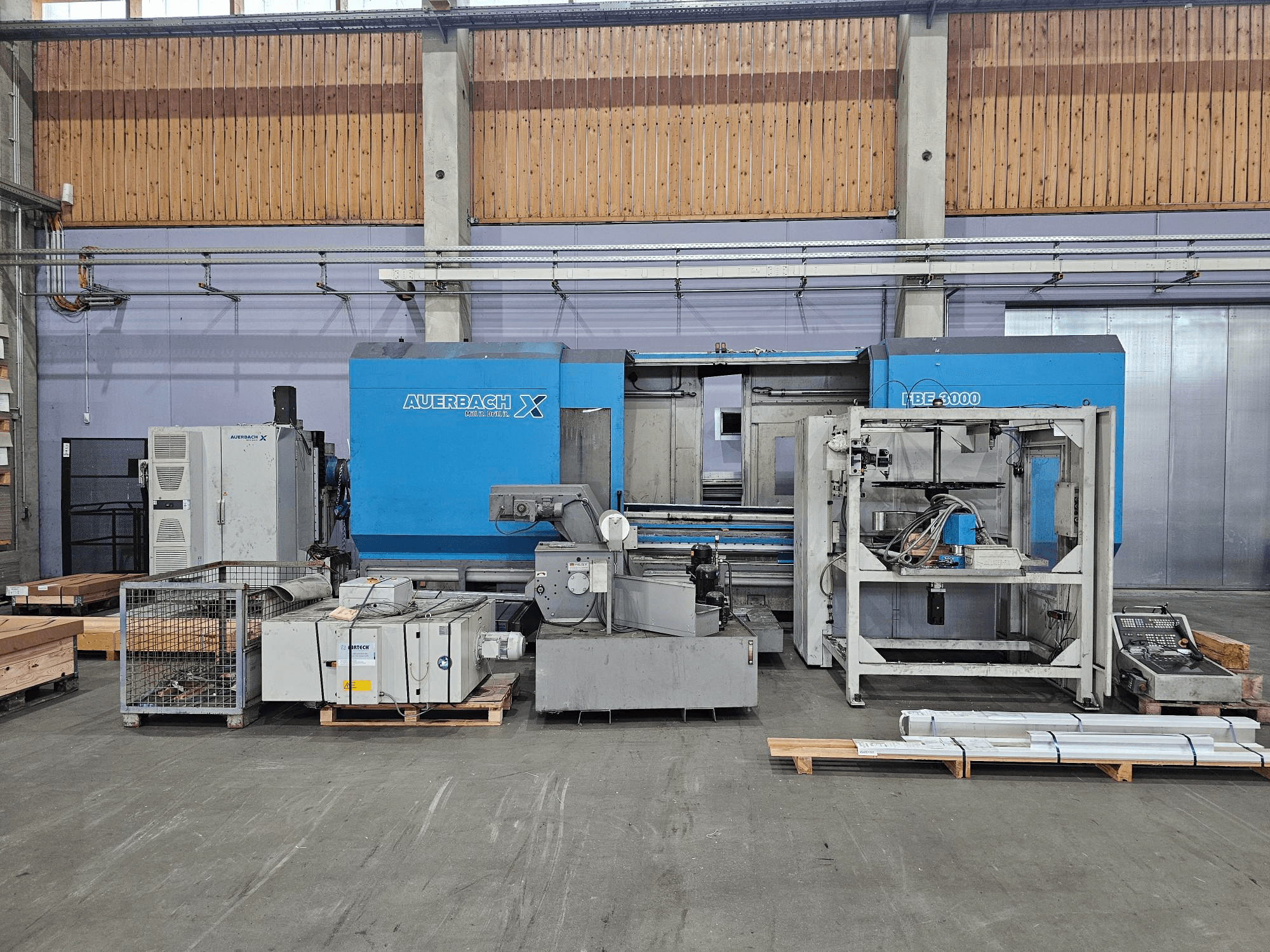 Auerbach X LBF-3000 machine in een fabrieksomgeving, zijaanzicht, met grijze en blauwe onderdelen en zichtbaar bedieningspaneel.