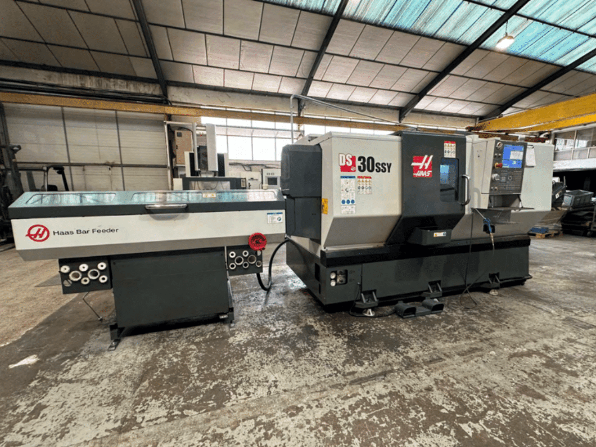 Haas DS-30SSY CNC-draaibank met Haas staveninvoer, zijaanzicht van bedieningspaneel en invoermechanisme in een werkplaats.