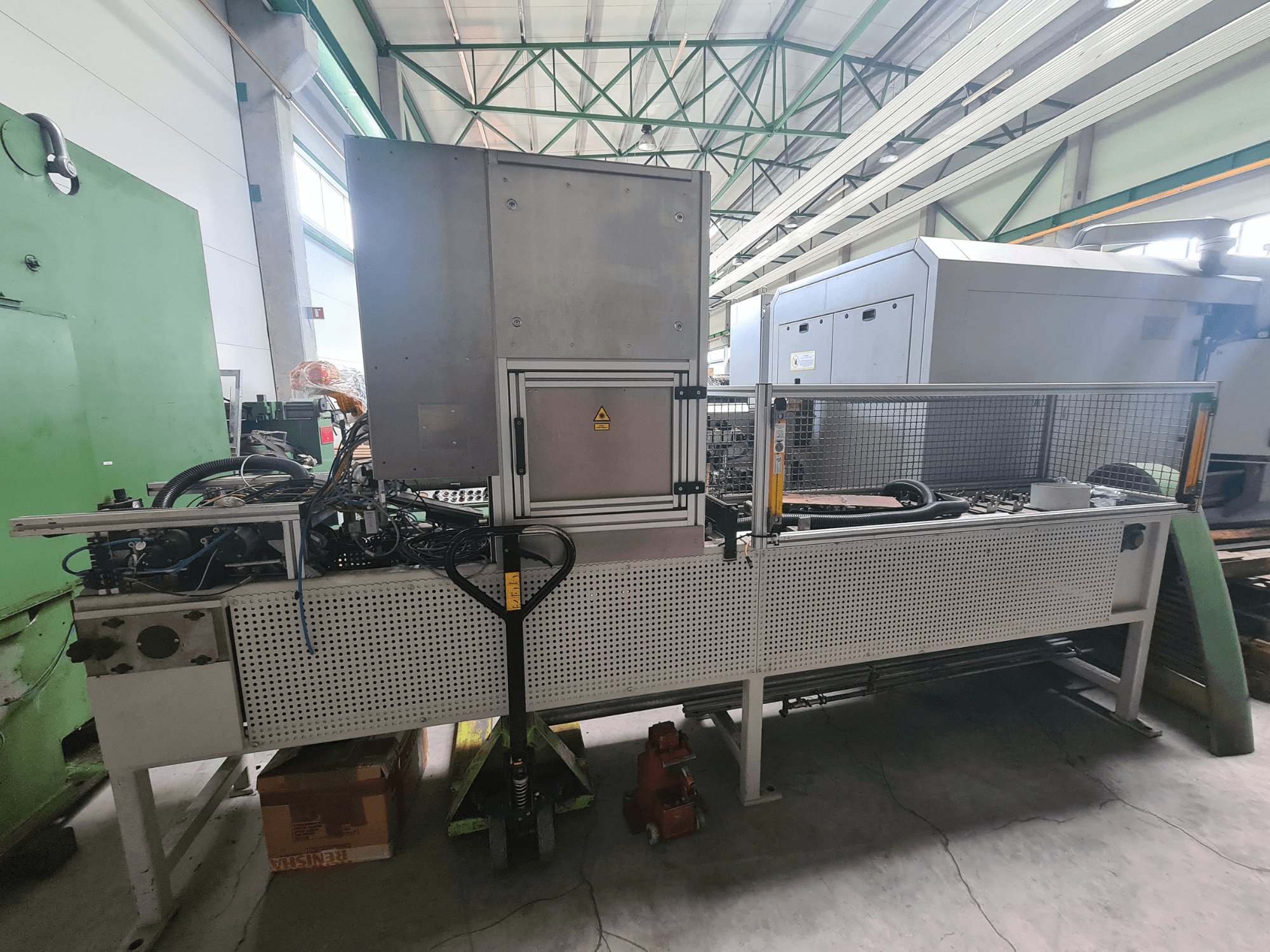 Industriële machines met een metalen frame, slangen en bedieningspaneel, gezien vanaf de zijkant in een fabrieksomgeving.