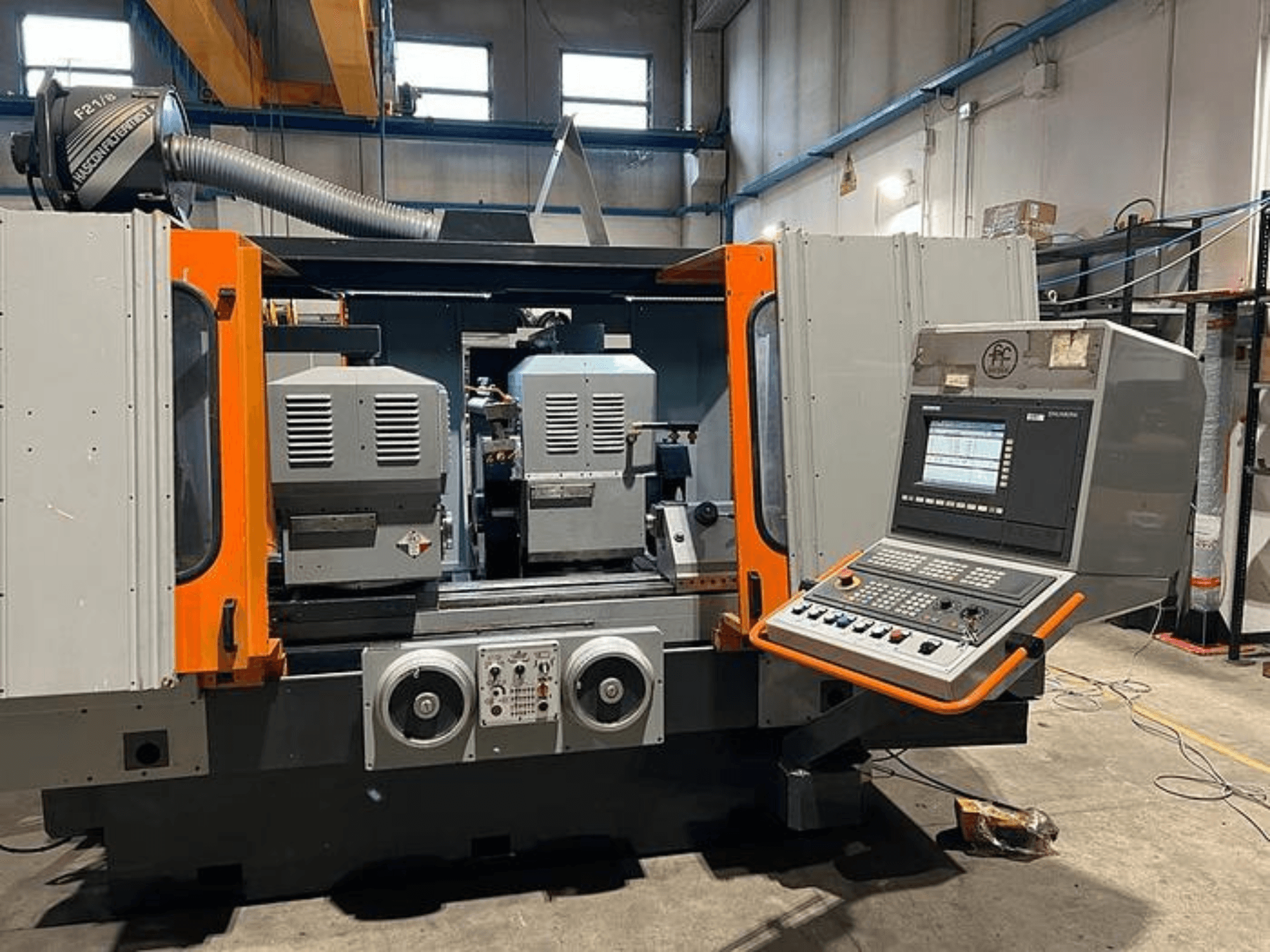 Vooraanzicht van een CNC machine met dubbele spindels, bedieningspaneel en oranje accenten. Voorzien van ventilatiekanaal en bedieningselementen.