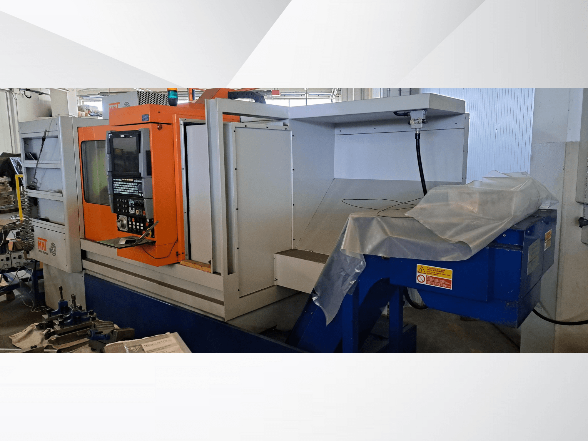 MNT CNC machine, vooraanzicht, met oranje bedieningspaneel, groot bewerkingsgebied en blauwe spanenafvoer.
