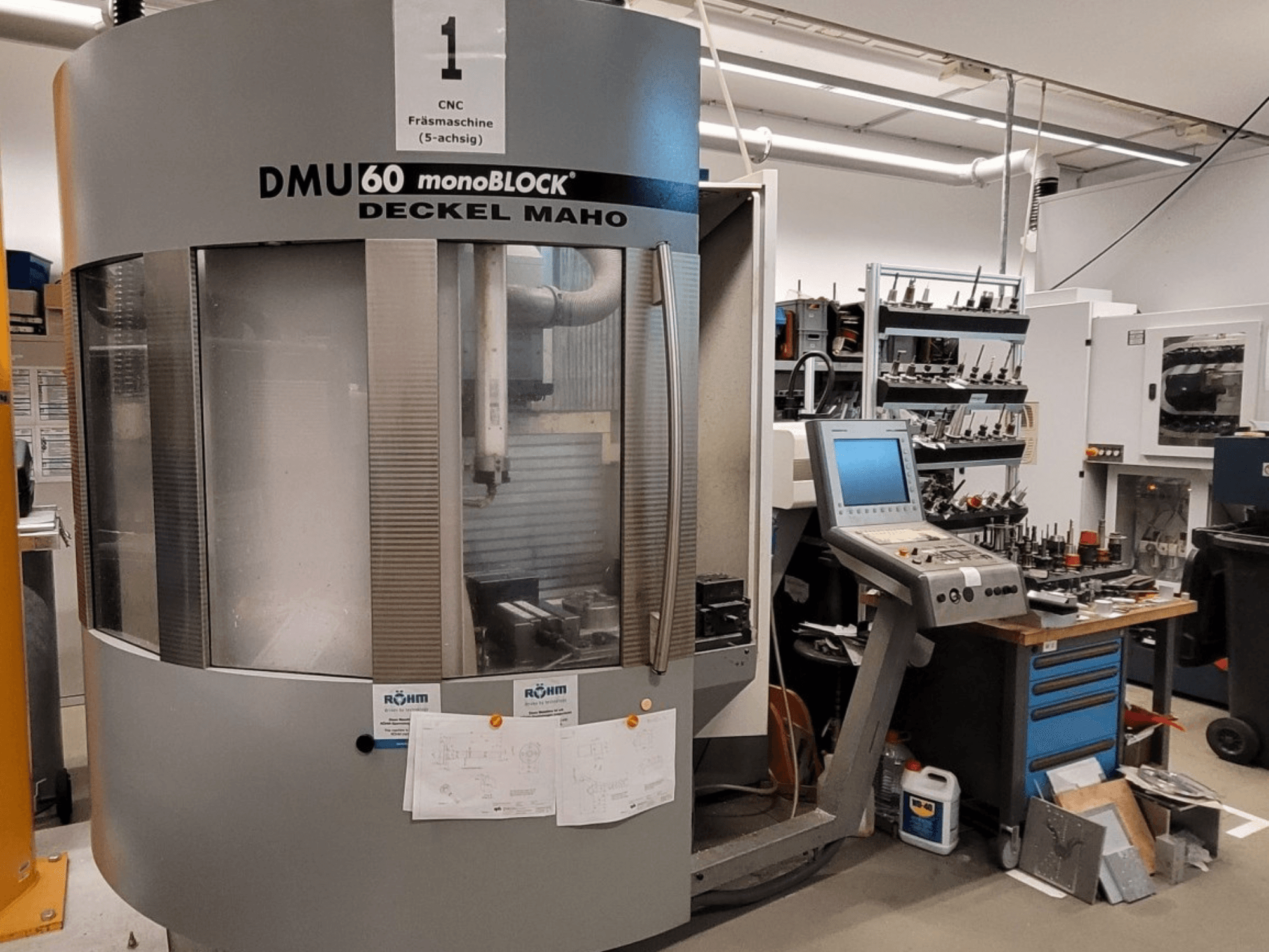 CNC freesmachine DECKEL MAHO DMU 60 monoBLOCK in vooraanzicht, met daarnaast het bedieningspaneel en de gereedschapopslag.