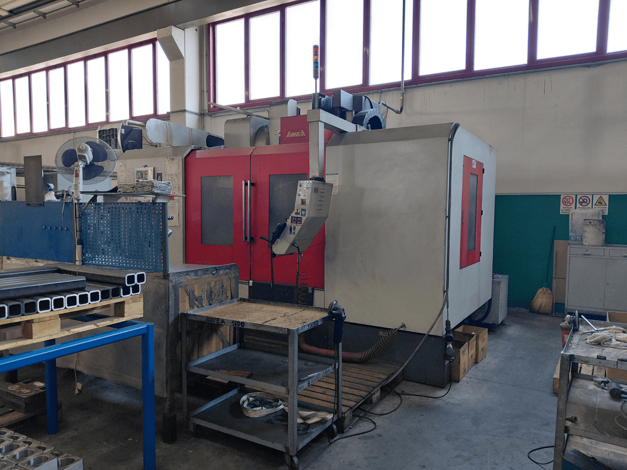 AWEA BM-1600 verticaal bewerkingscentrum, vooraanzicht, met rode en grijze behuizing; de werkbank en het gereedschap ernaast zijn zichtbaar.