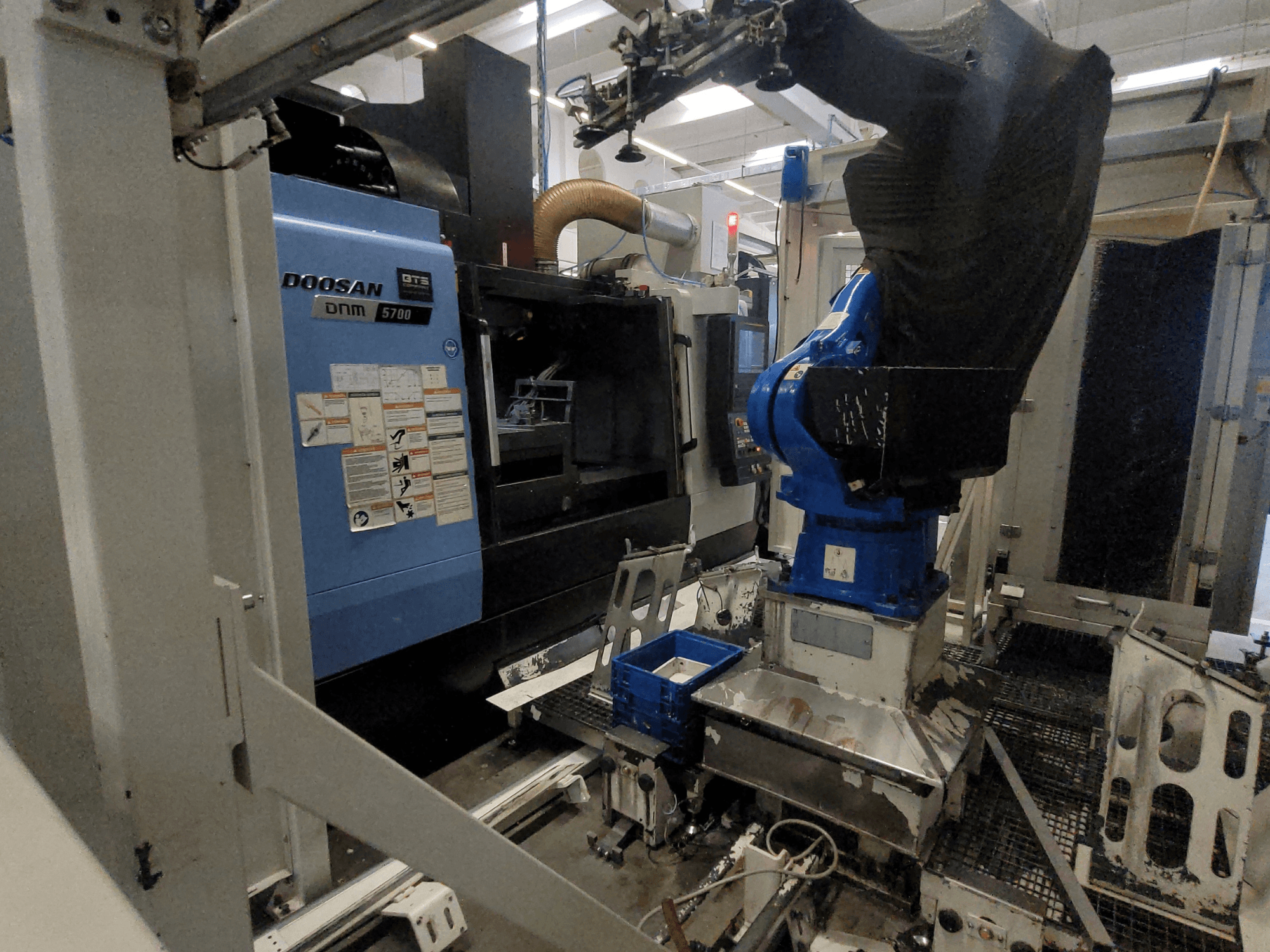 Het verticale bewerkingscentrum DOOSAN DNM 5700 in een fabrieksomgeving, met een blik op de voorkant en de geïntegreerde robotarm.