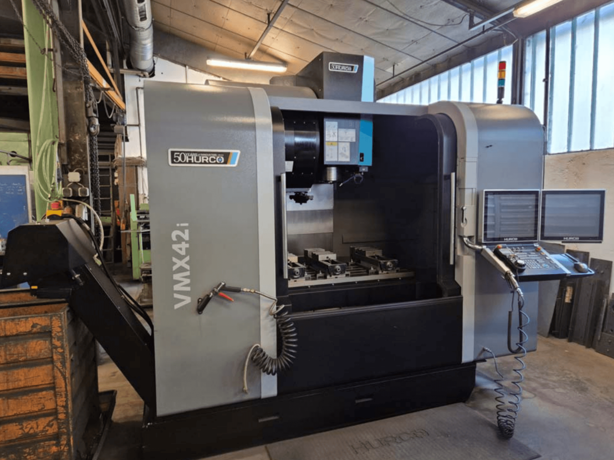 Hurco VMX 42i verticaal bewerkingscentrum, vooraanzicht, met bedieningspaneel en werkgebied met bankschroeven.