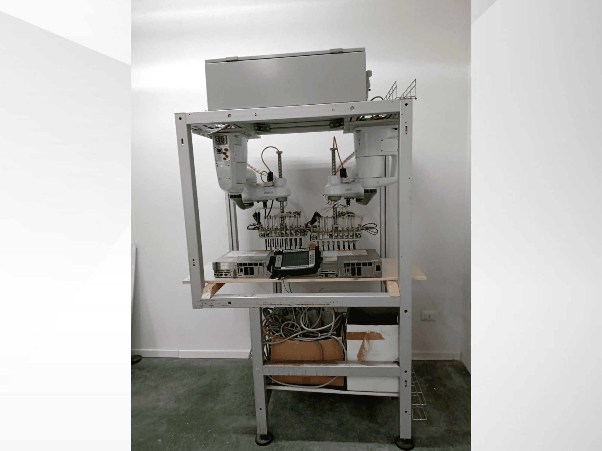 Geautomatiseerd robotwerkstation met twee armen, beeldscherm en elektronica op een metalen frame, vooraanzicht, geavanceerde technologische opstelling.