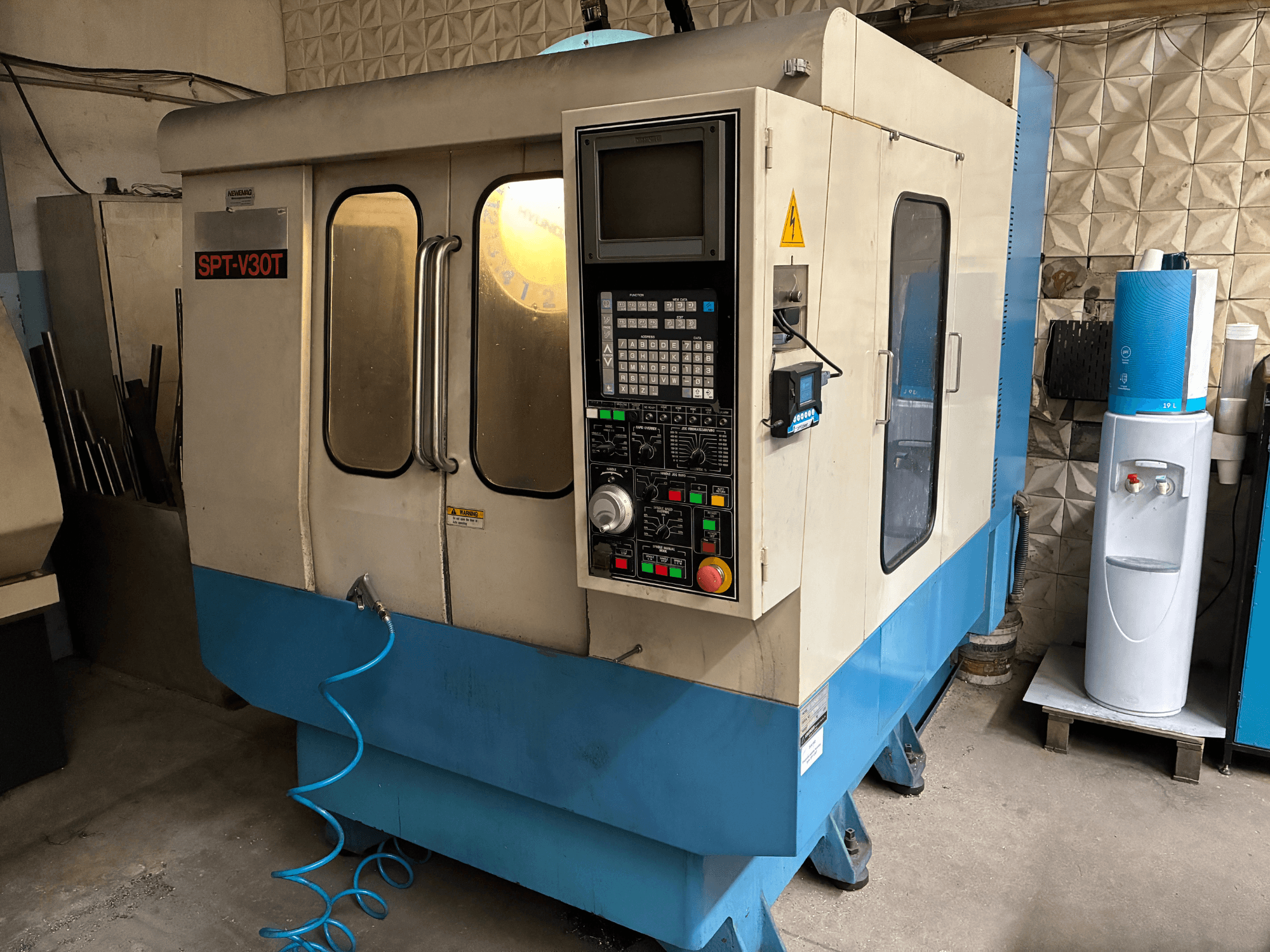 SPT-V30T CNC machine in blauw en wit, vooraanzicht met bedieningspaneel, deuren en luchtslang. Perfect voor precisiebewerking.