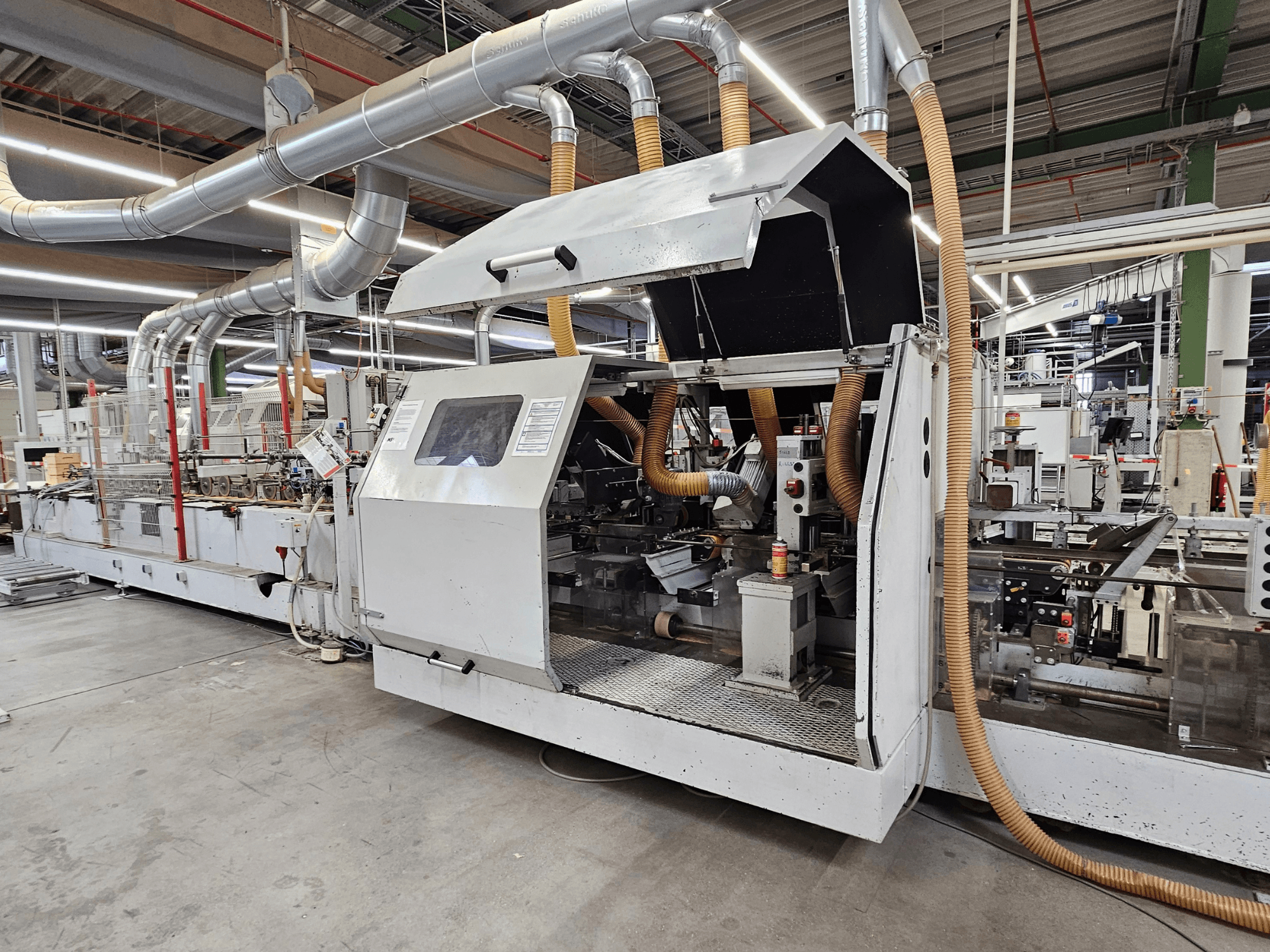 HOMAG FG63 kantenbewerkingsmachine in een fabrieksomgeving, zijaanzicht met operationele componenten en stofafzuigsysteem.