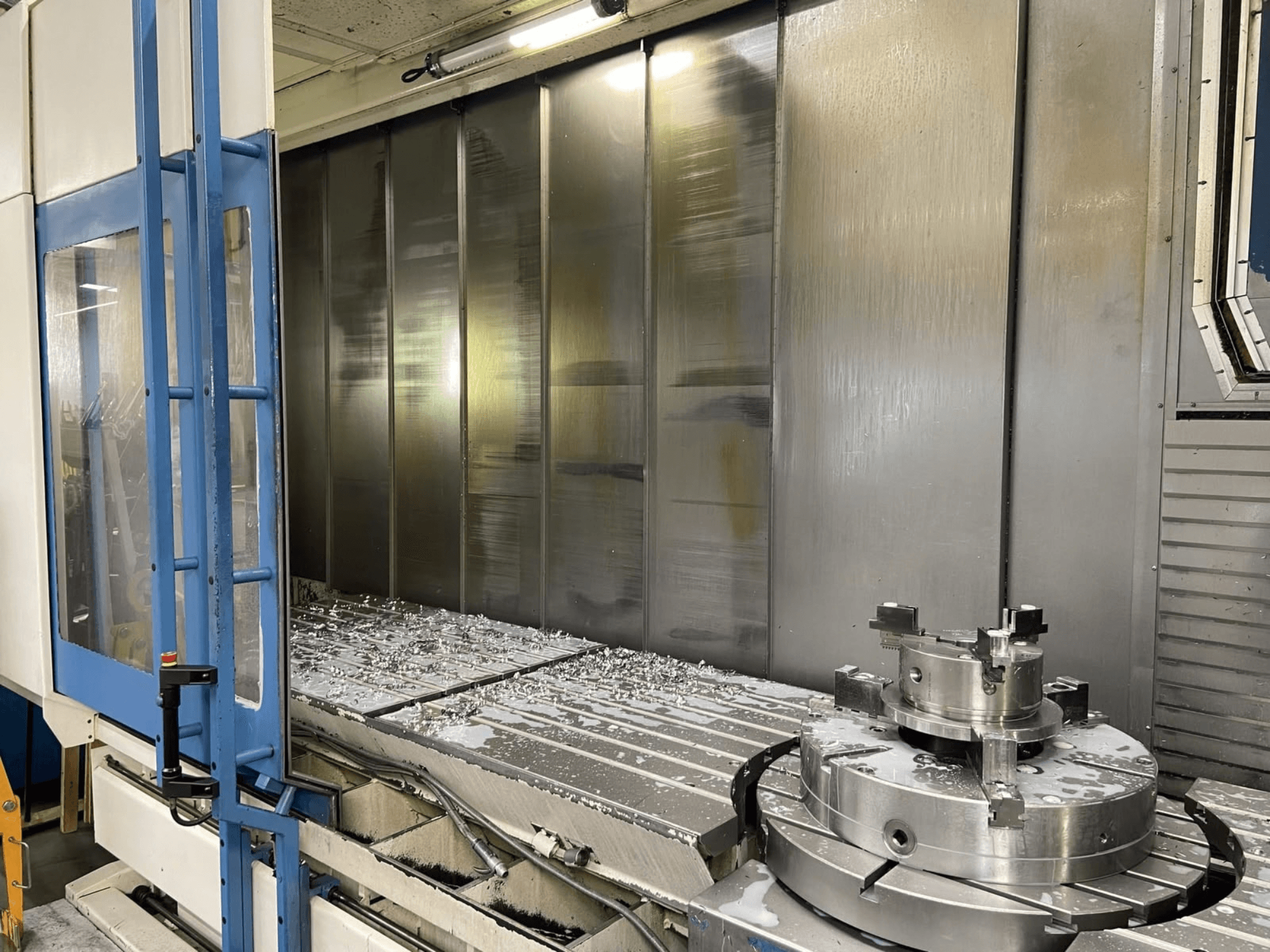 AXA VHC-3-3000-M/E verticaal bewerkingscentrum, vooraanzicht, met daarop te zien: gefreesde metaalspaanders op de werktafel en snijgereedschappen.