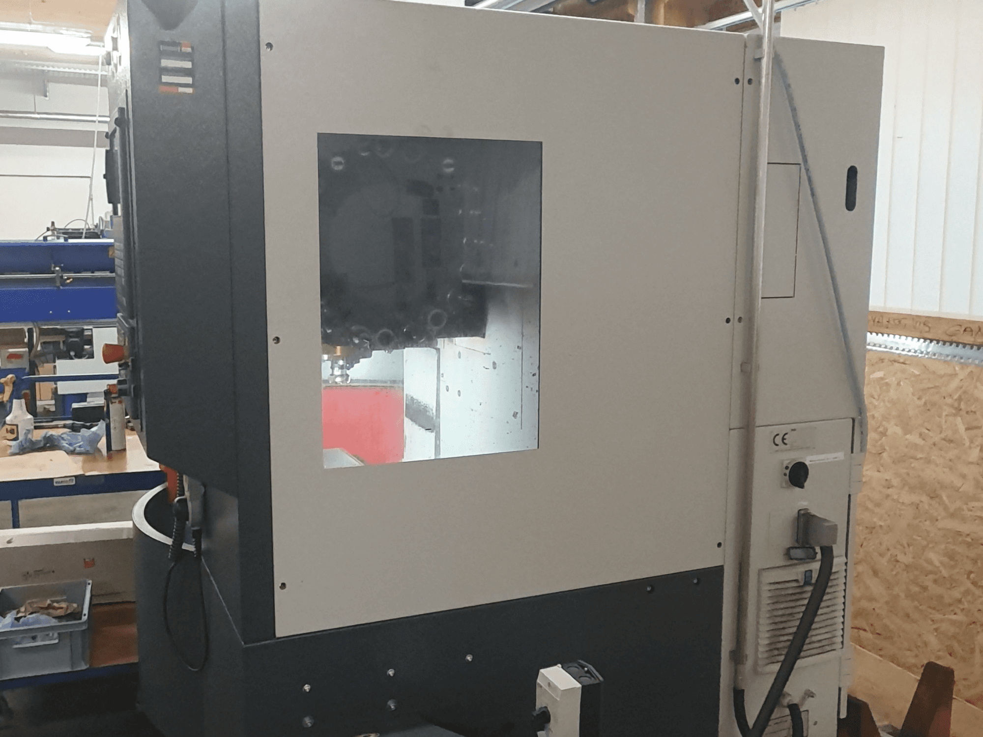 Zijaanzicht van een metaalbewerkingsmachine met zichtbaar bedieningspaneel, groot kijkvenster en ingewikkelde interne onderdelen.