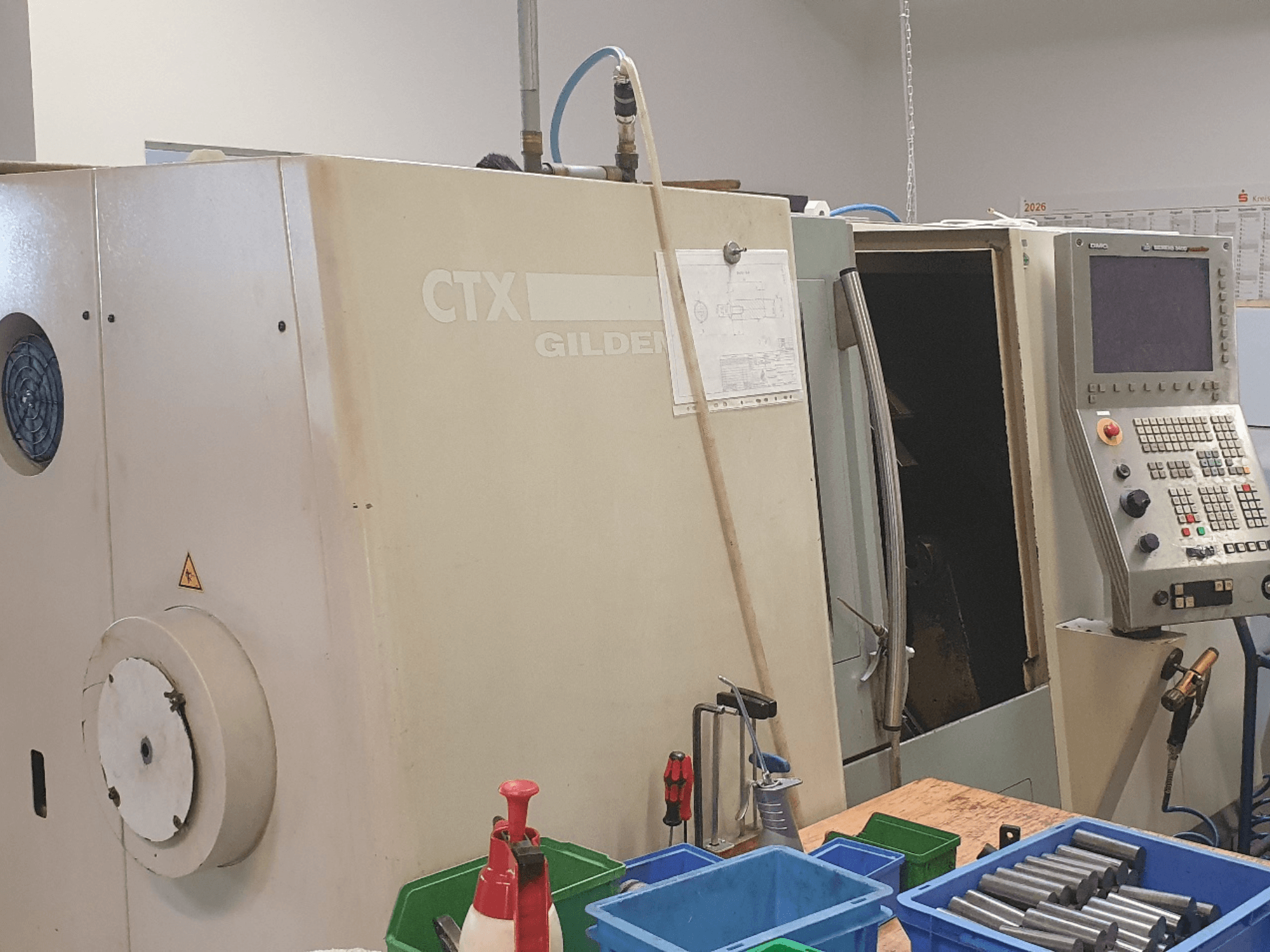Vooraanzicht van de DMG GILDEMEISTER CTX 310 horizontale draaibank, met zichtbaar bedieningspaneel en gereedschappen en bakken op de voorgrond.