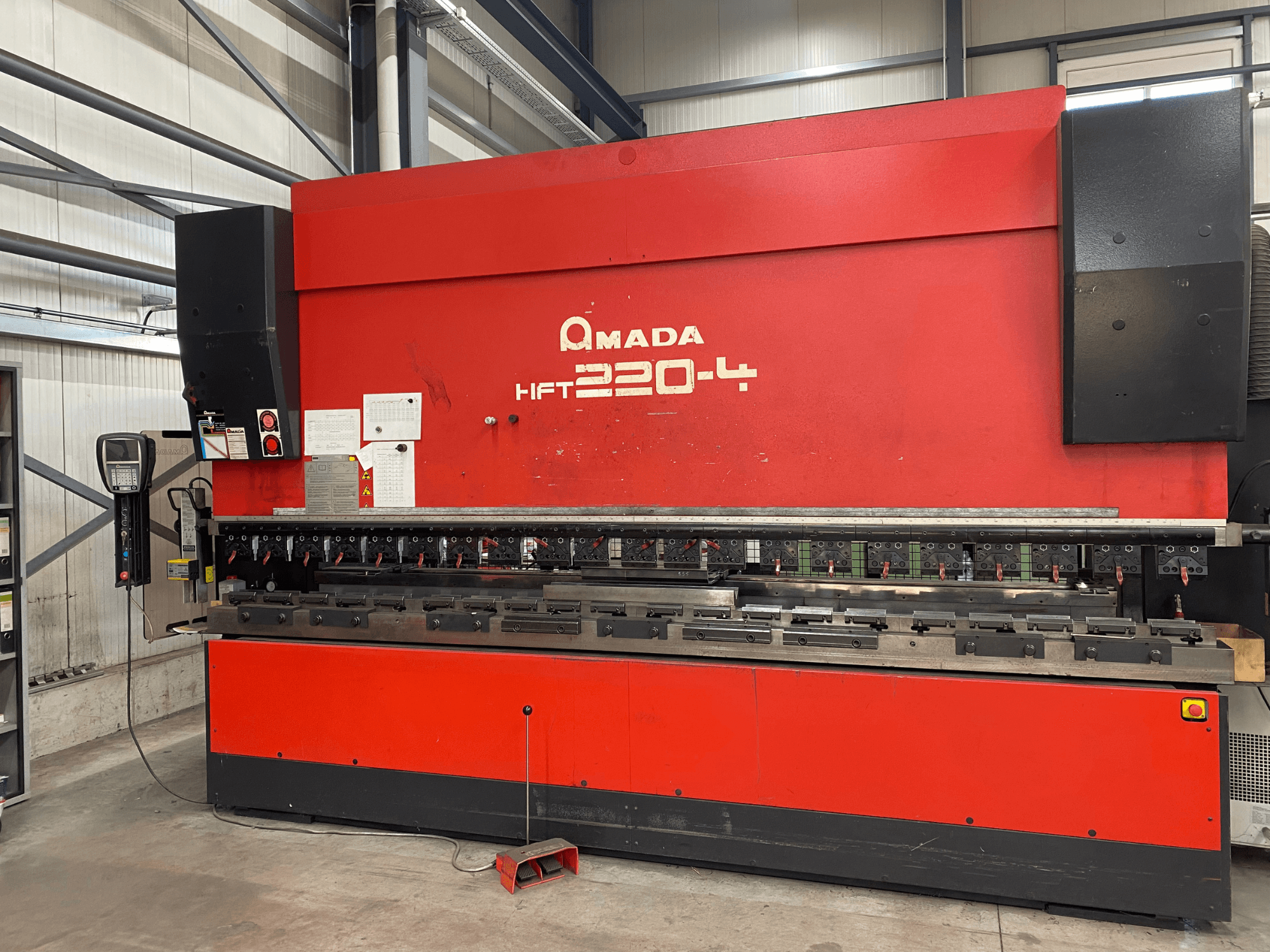 Rode AMADA HFT 220-4 afkantpers in een fabrieksopstelling, vooraanzicht met het bedieningspaneel en de buiggereedschappen op het werkvlak.