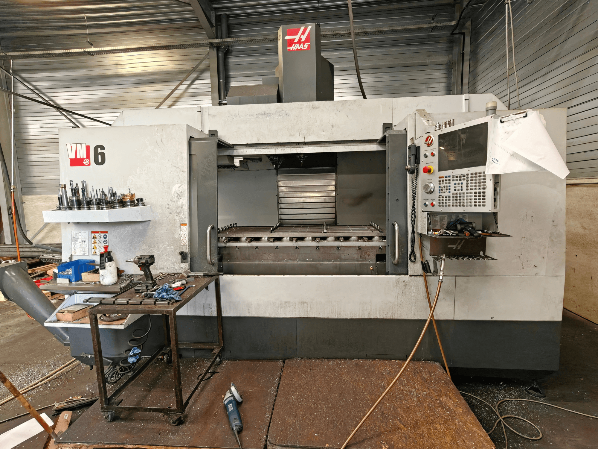 Haas VM-6 verticaal bewerkingscentrum, vooraanzicht, met zichtbaar gereedschapmagazijn, bedieningspaneel en vuil in het werkgebied.